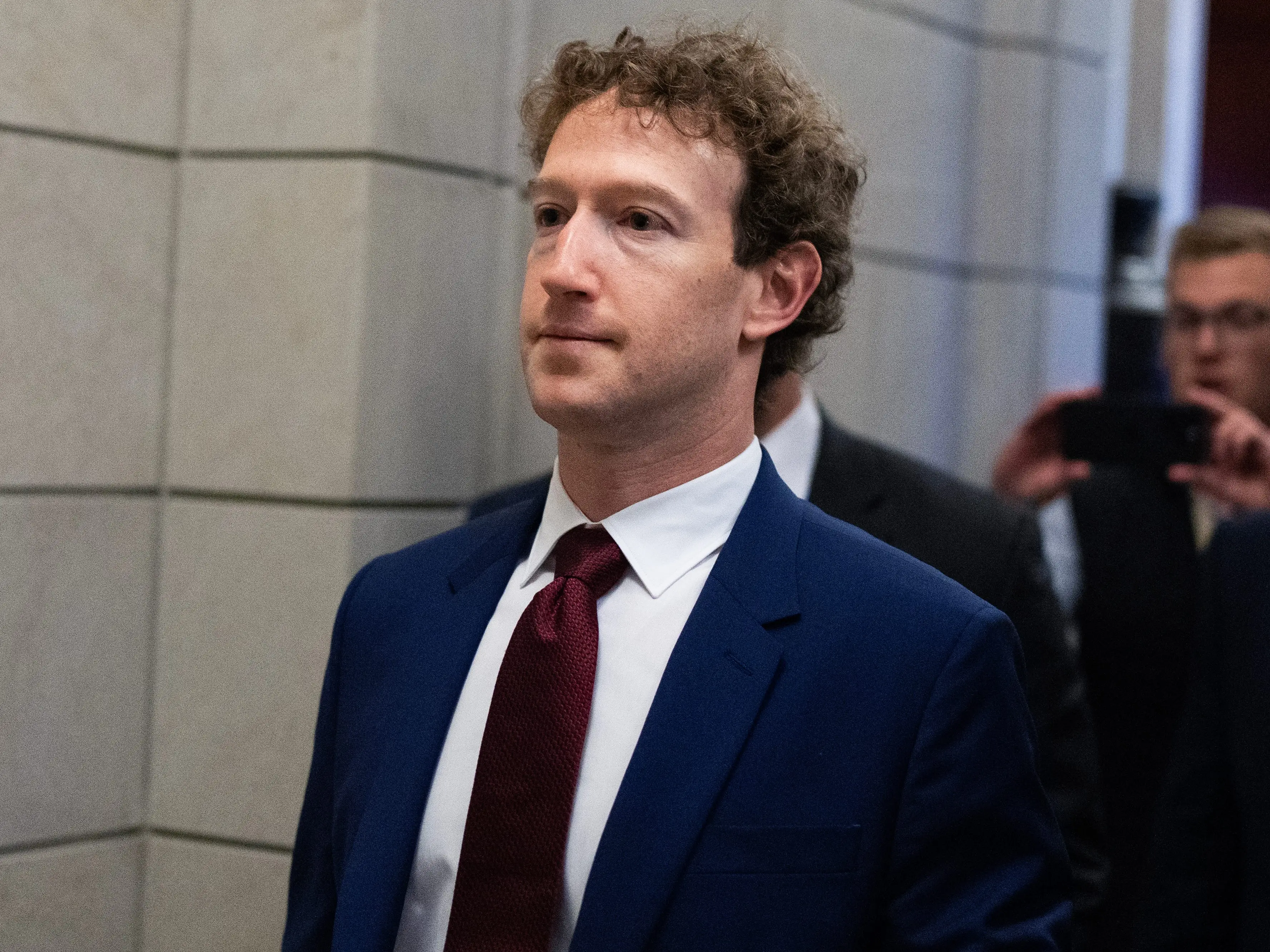 Mark Zuckerberg wears a navy suit and burgundy tie walking at the US Capitol.