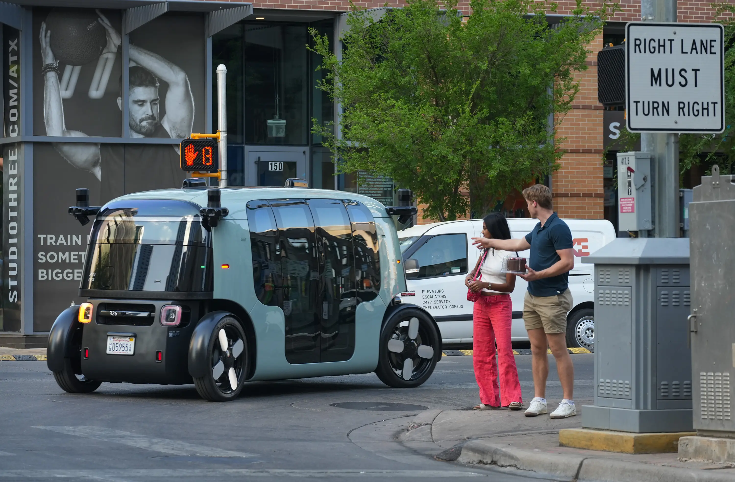 Pedestrians watch as a Zoox robotaxi passes along East Fifth Street in Austin on Wednesday, March 25, 2026. Zoox began testing the vehicle on Austin streets this week.