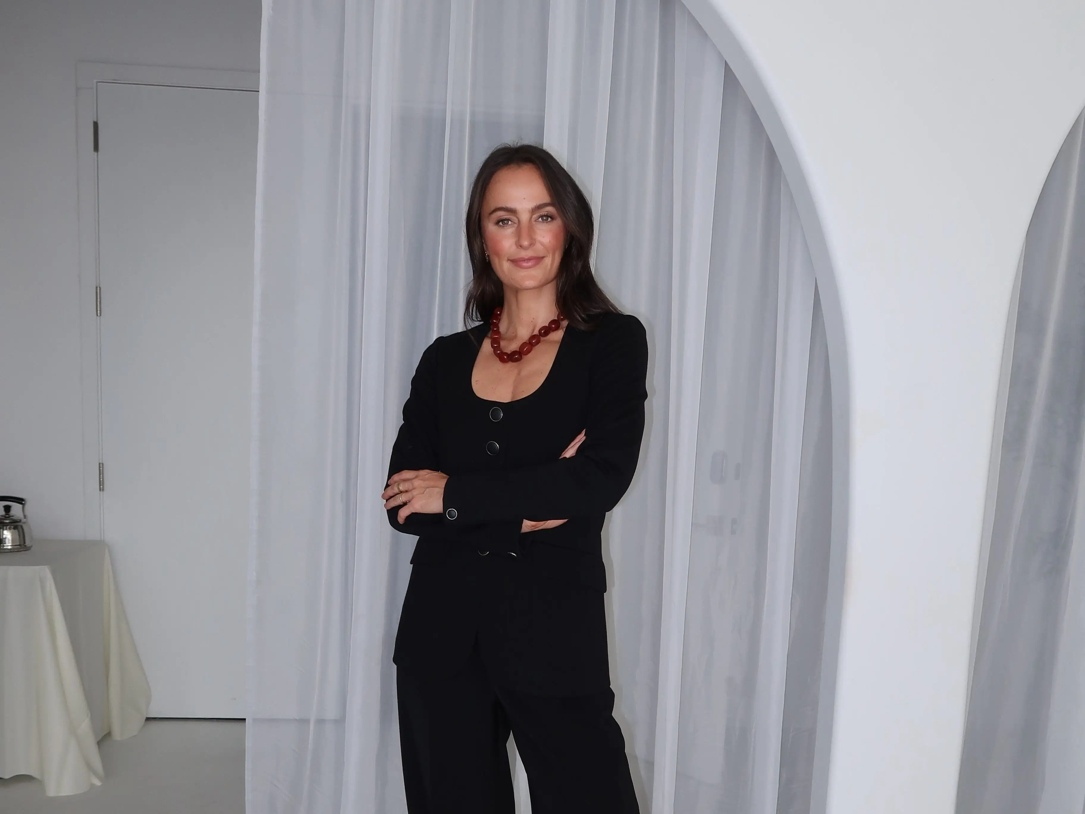 A woman wears all black and stands in a white room.