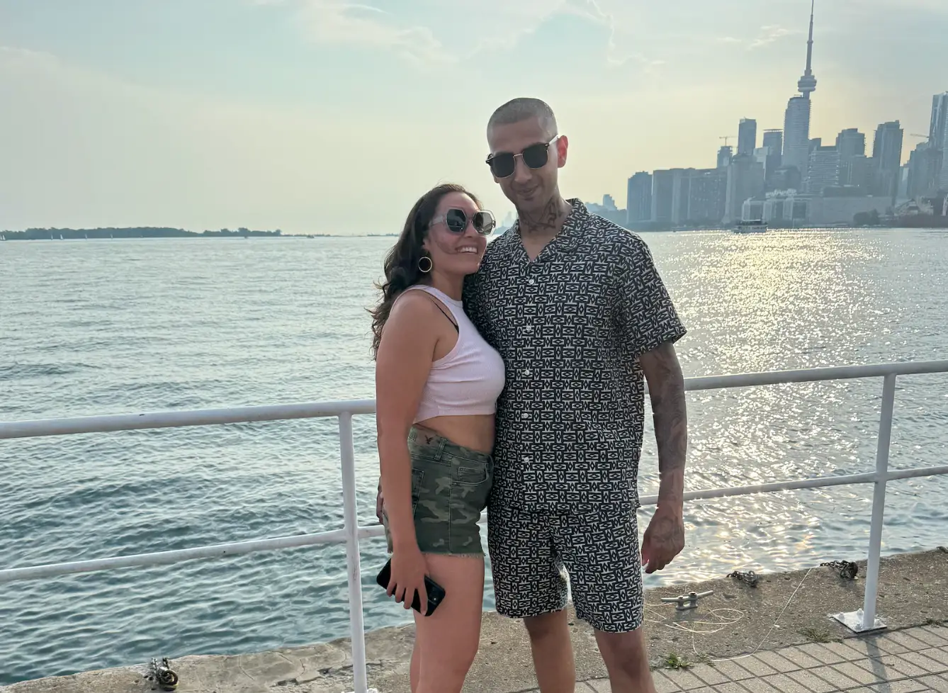 The writer standing next to her husband near the water with the Toronto skyline in the background.