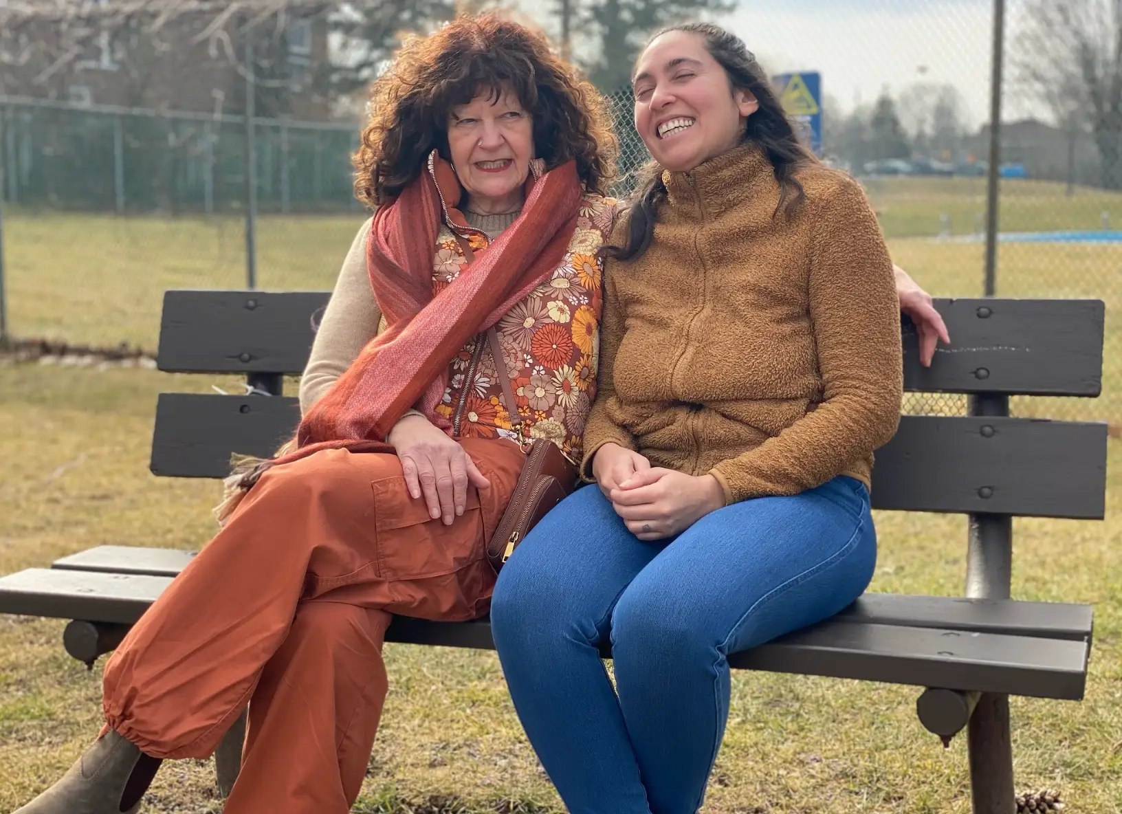 The writer sitting on a brown bench next to her neighbor, with a park in the background.