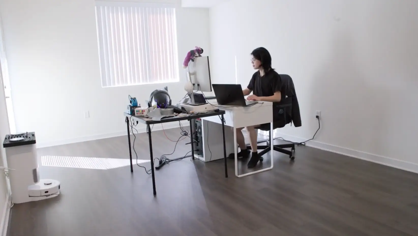 Raymond Zeng in his minimally furnished apartment that has one desk and one roomba.