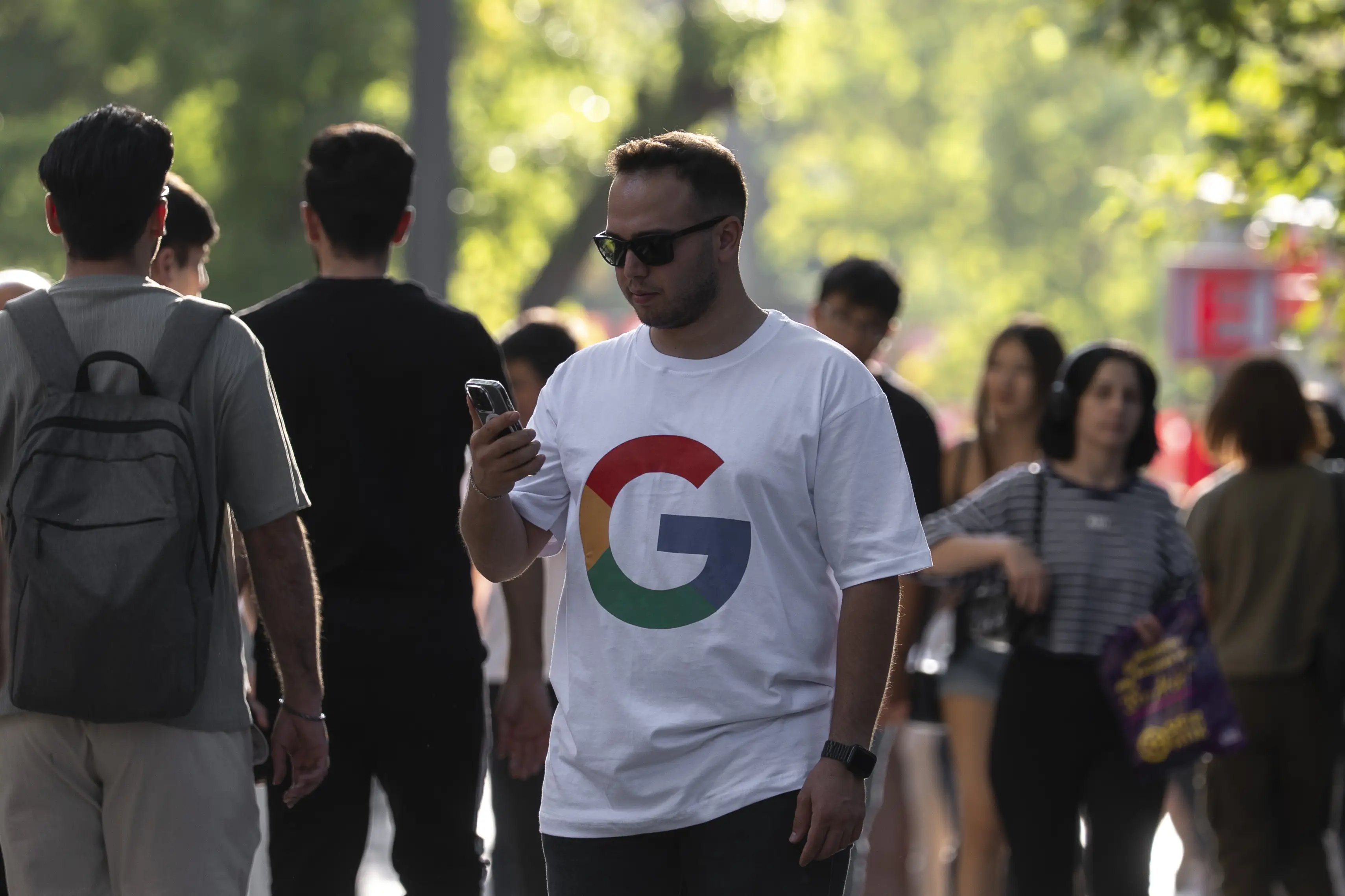 Man stands in crowd with a Google logo shirt and a mobile phone in his hand