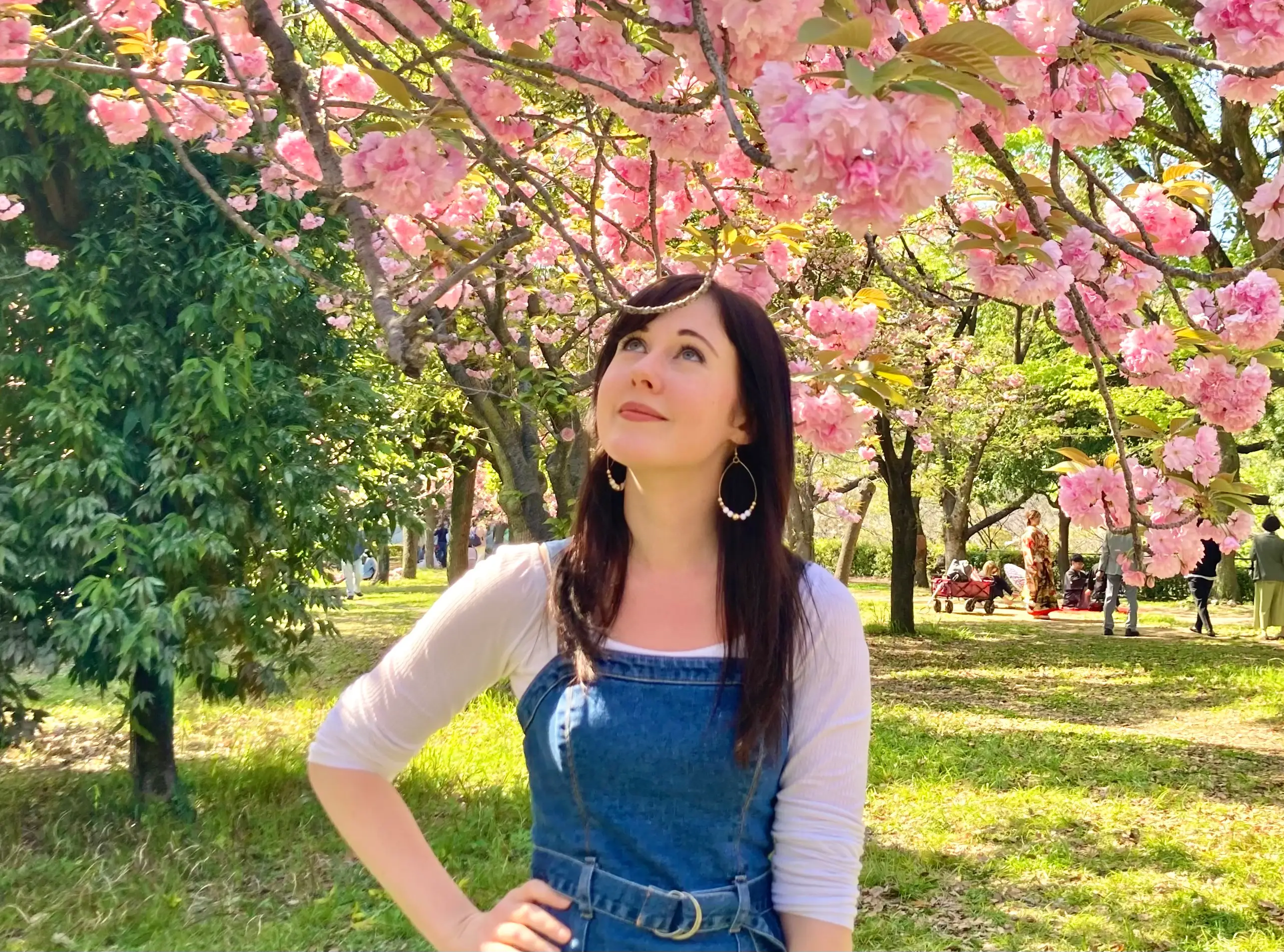 Woman smiling up at pink blossoming flowers in garden