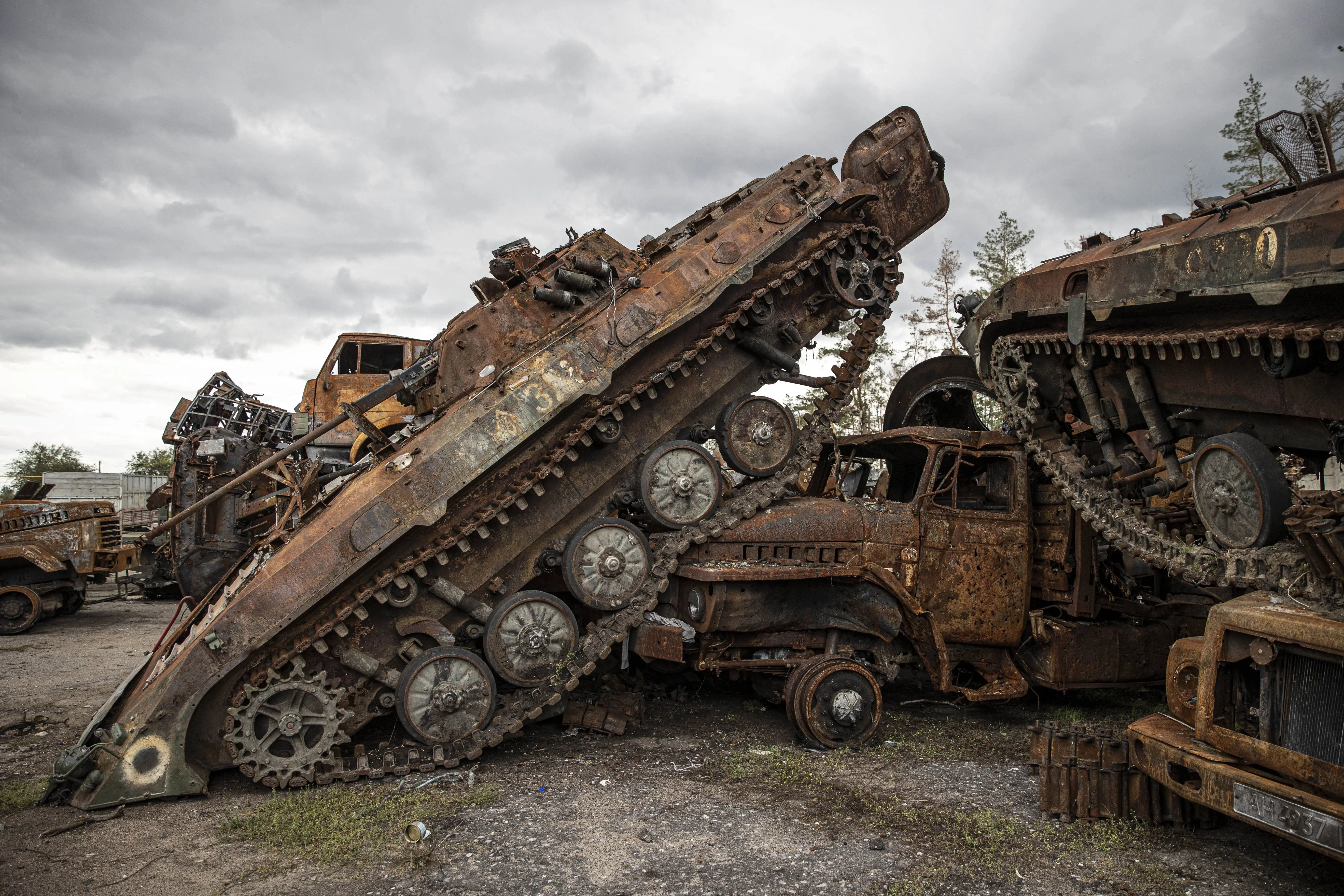 Rusted tanks, including one balanced on its nose, on tarmac under a grey sky