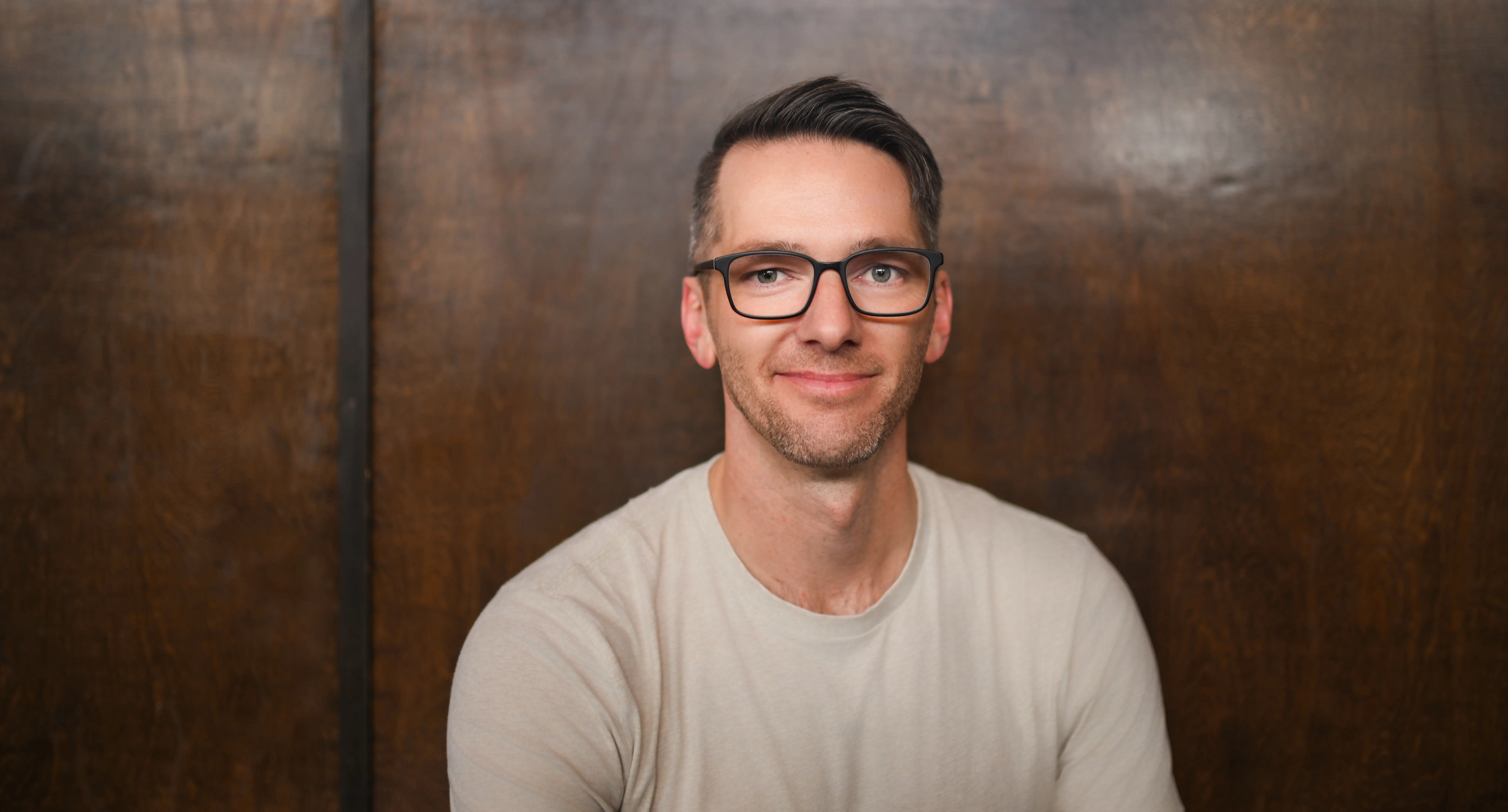 A man smiles in front a wooden background.