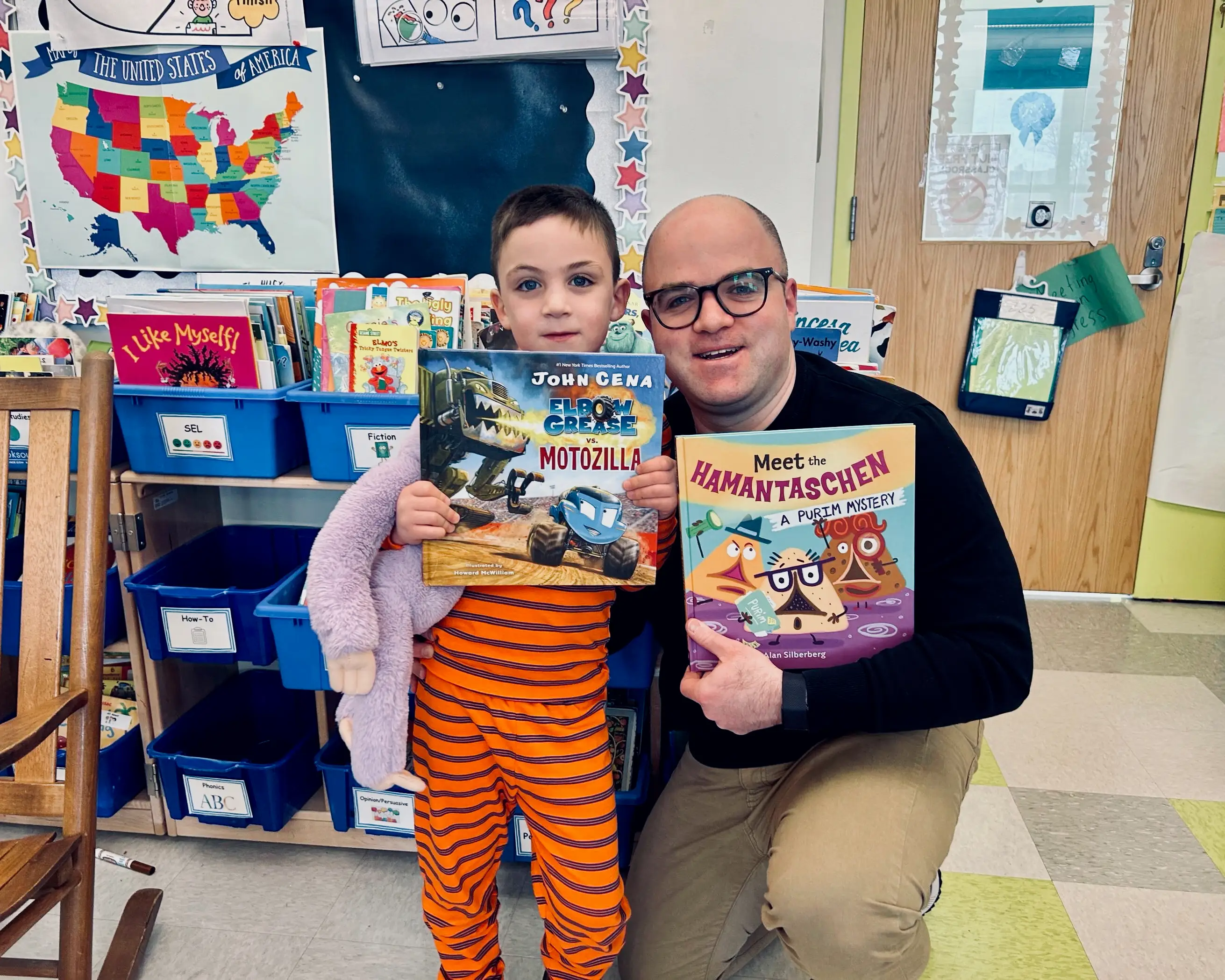 The author holds up a book with his child while reading in the classroom.