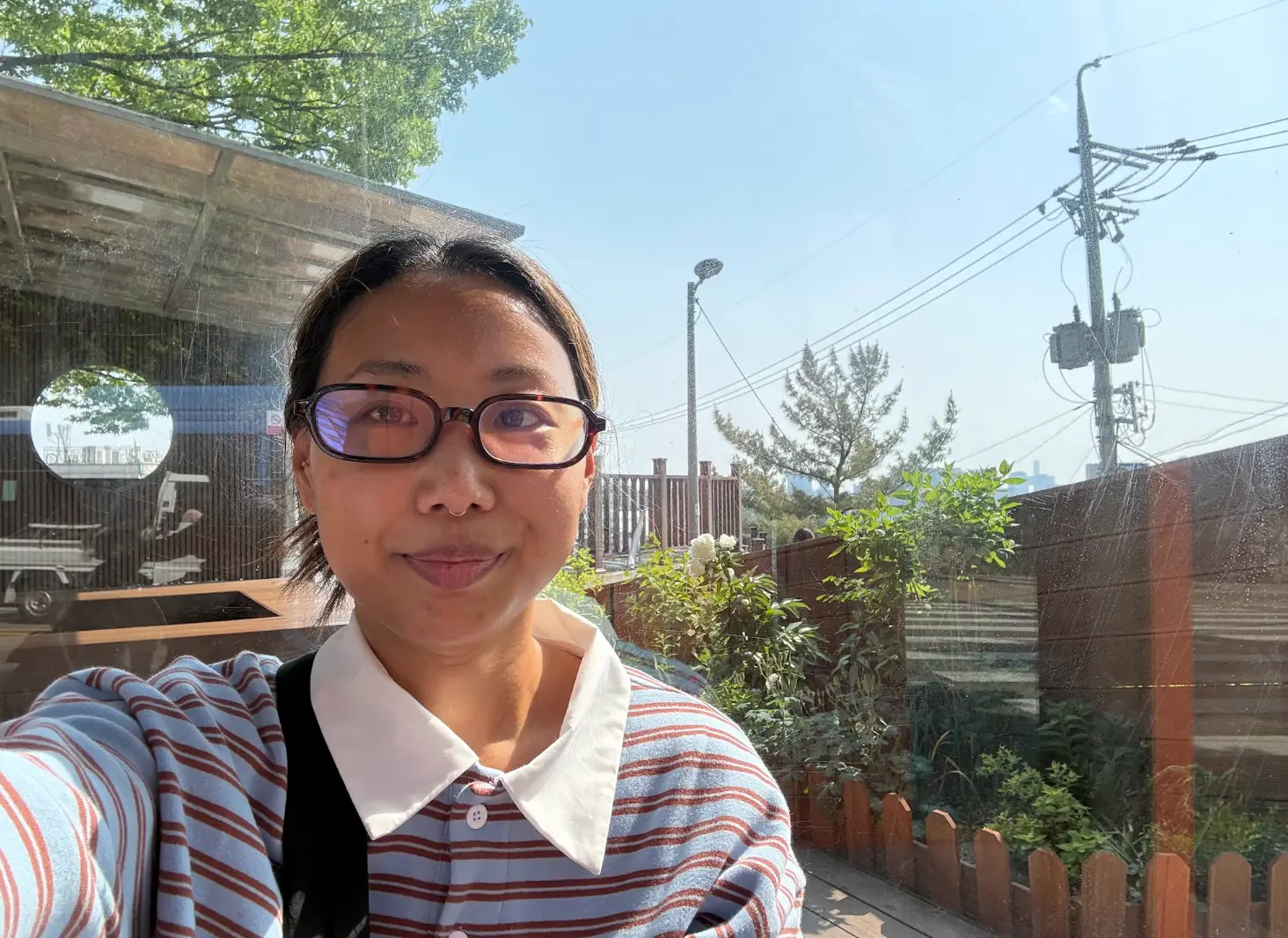 The writer wearing a striped shirt and standing in front of plants in Haebangchon, Seoul.