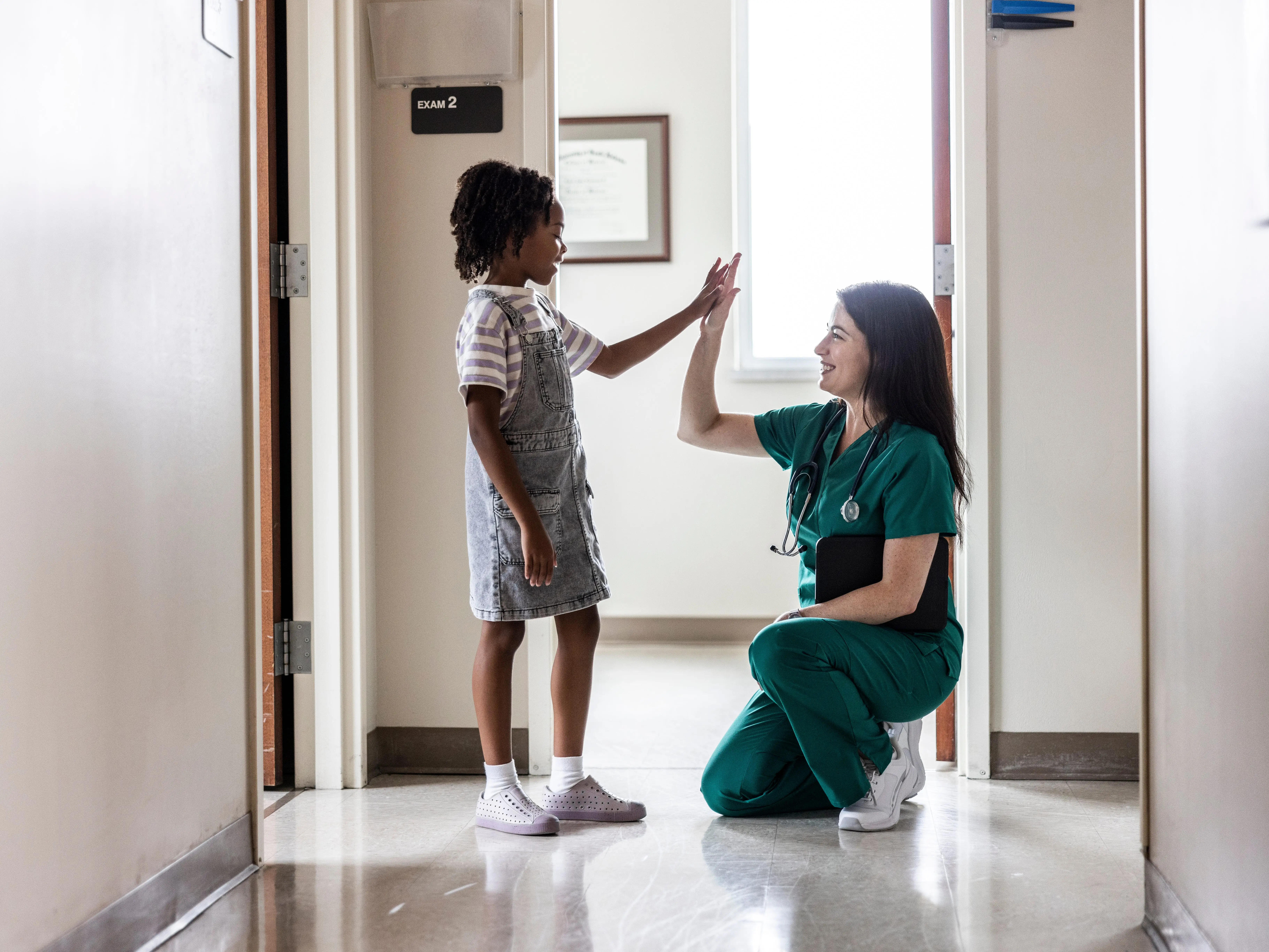 A healthcare worker and a child high-fiving outside an exam room