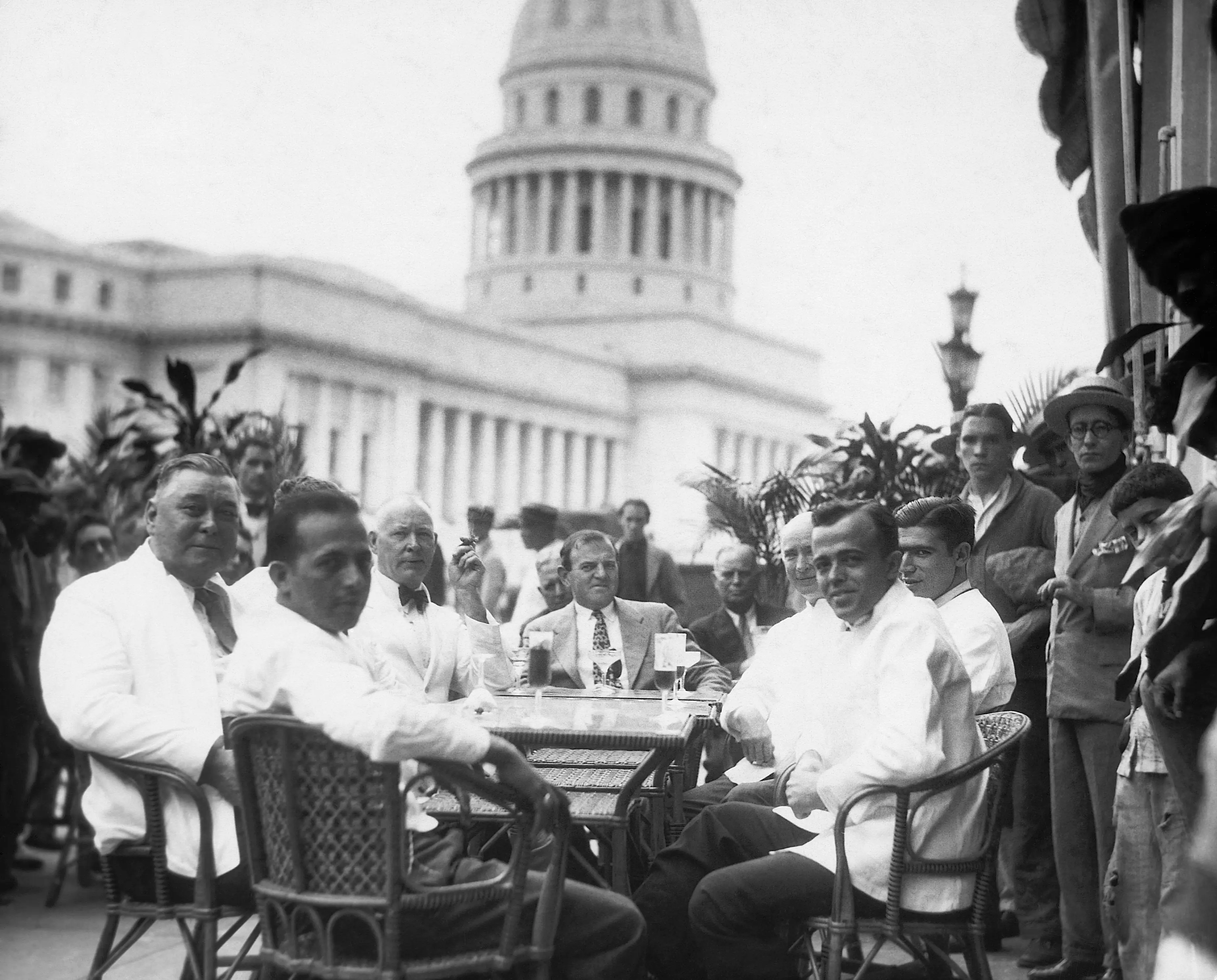 Havana, Cuba: An outdoor cafe with a view of the Capitol Building in the background. Men are seated in the cafe enjoying refreshing beverages. Photograph, circa 1940's-1950's.