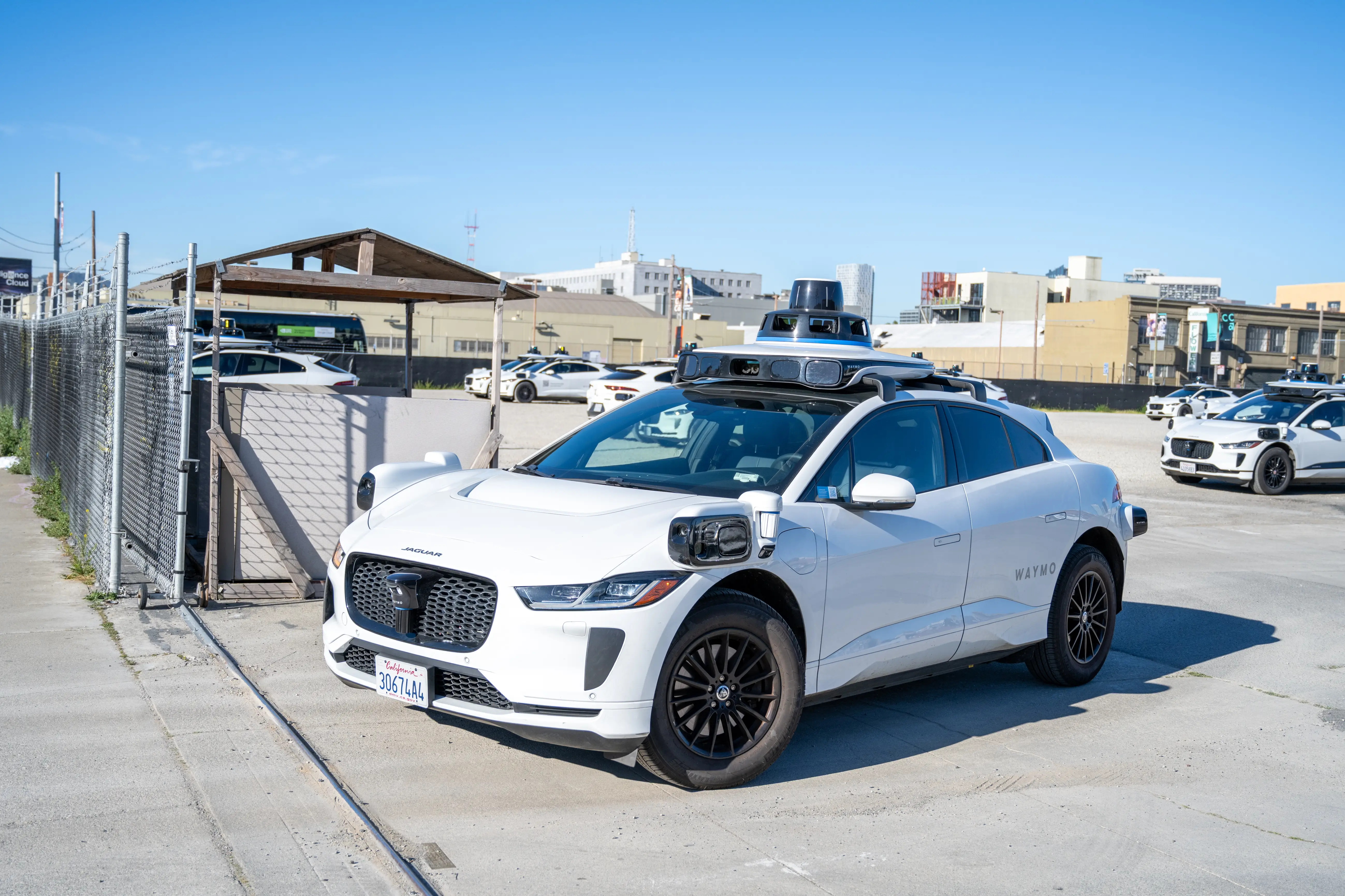 A white self-driving Waymo car, with cameras and other sensors on its roof and its sides, pulls out of a parking lot in San Francisco.