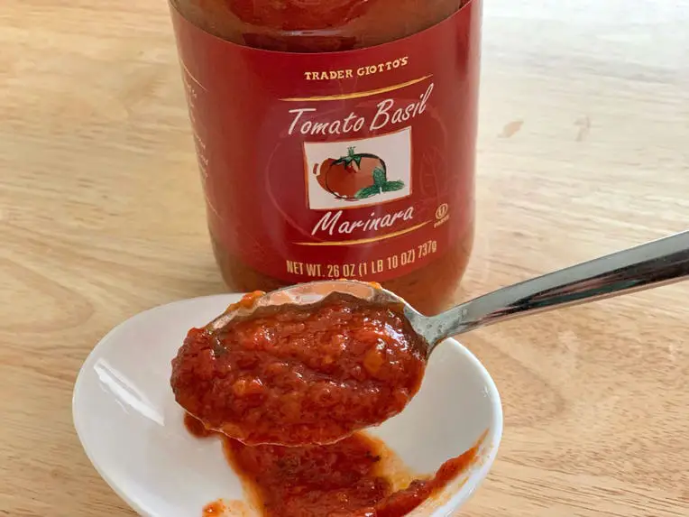 A spoonful of marinara sauce in front of a jar of Trader Joe's tomato-basil marinara.