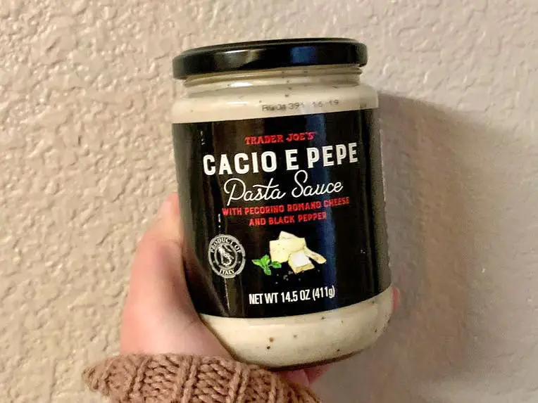 A hand holding a jar of Trader Joe's cacio e pepe sauce.