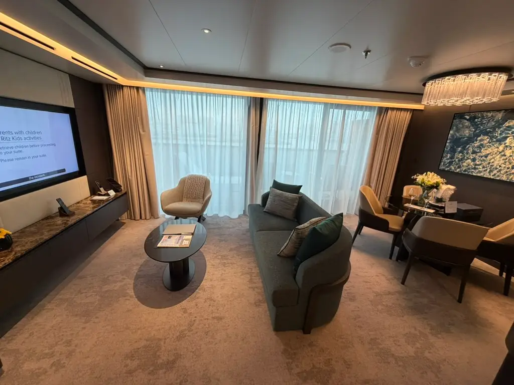 View of couch with coffee table in front of TV with dining table behind it and large floor-to-ceiling windows