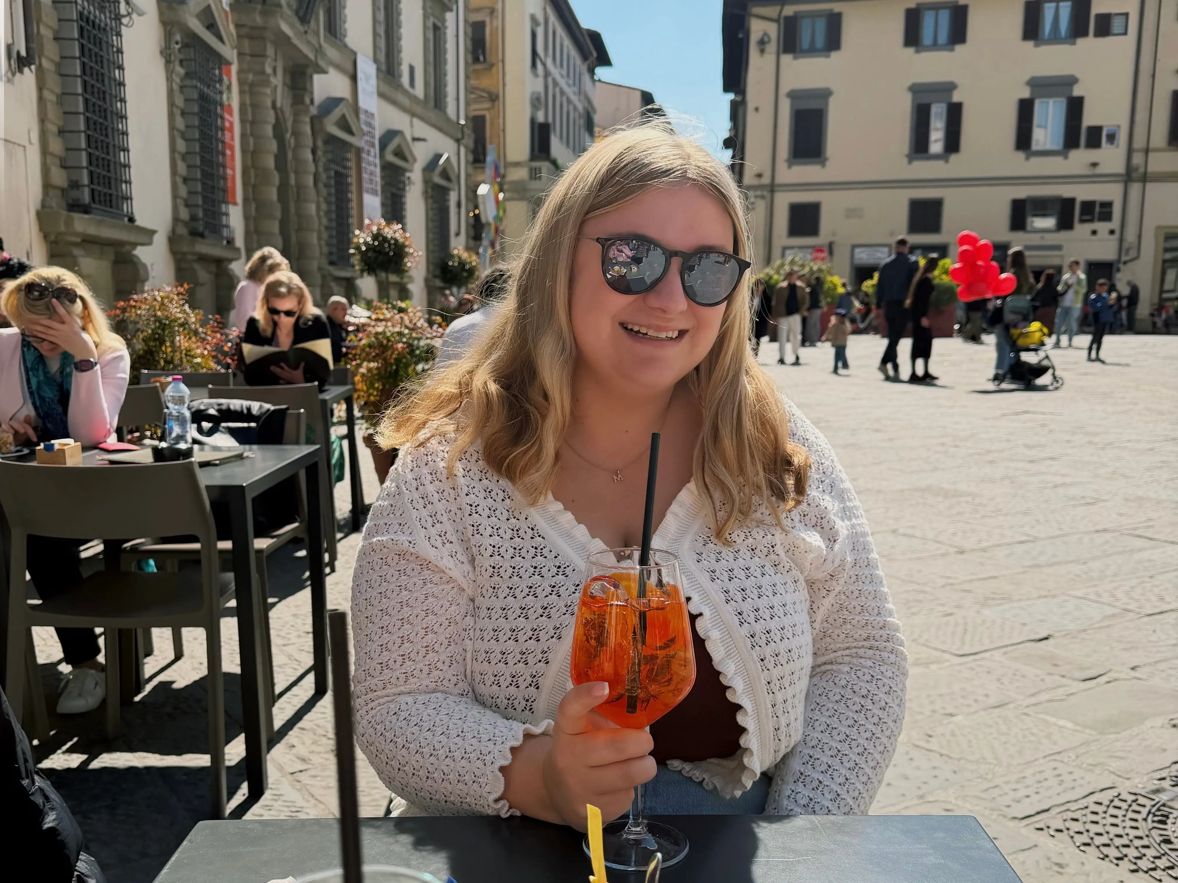The writer wearing a white sweater and drinking an Aperol Spritz in Florence, Italy.