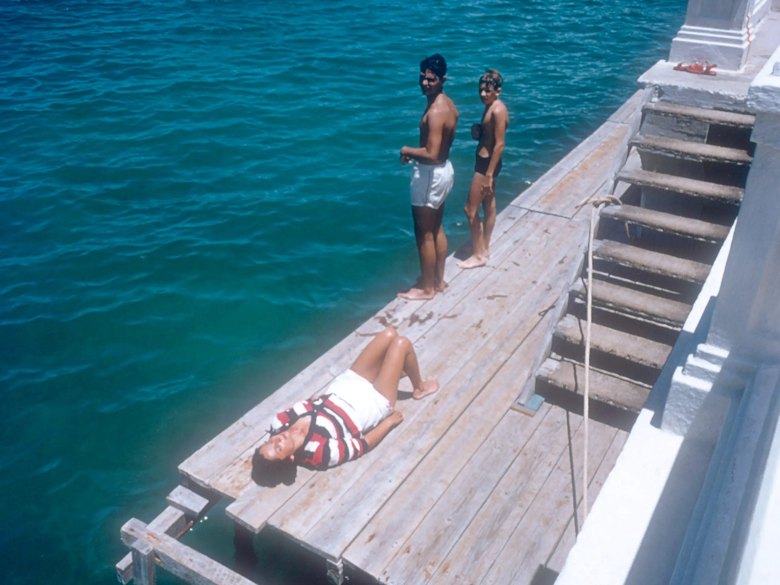 HAVANA, CUBA - AUGUST, 1955: General view of two boys looking at a woman lying on a deck and sunbathing near the beach circa August, 1955 in Havana, Cuba.