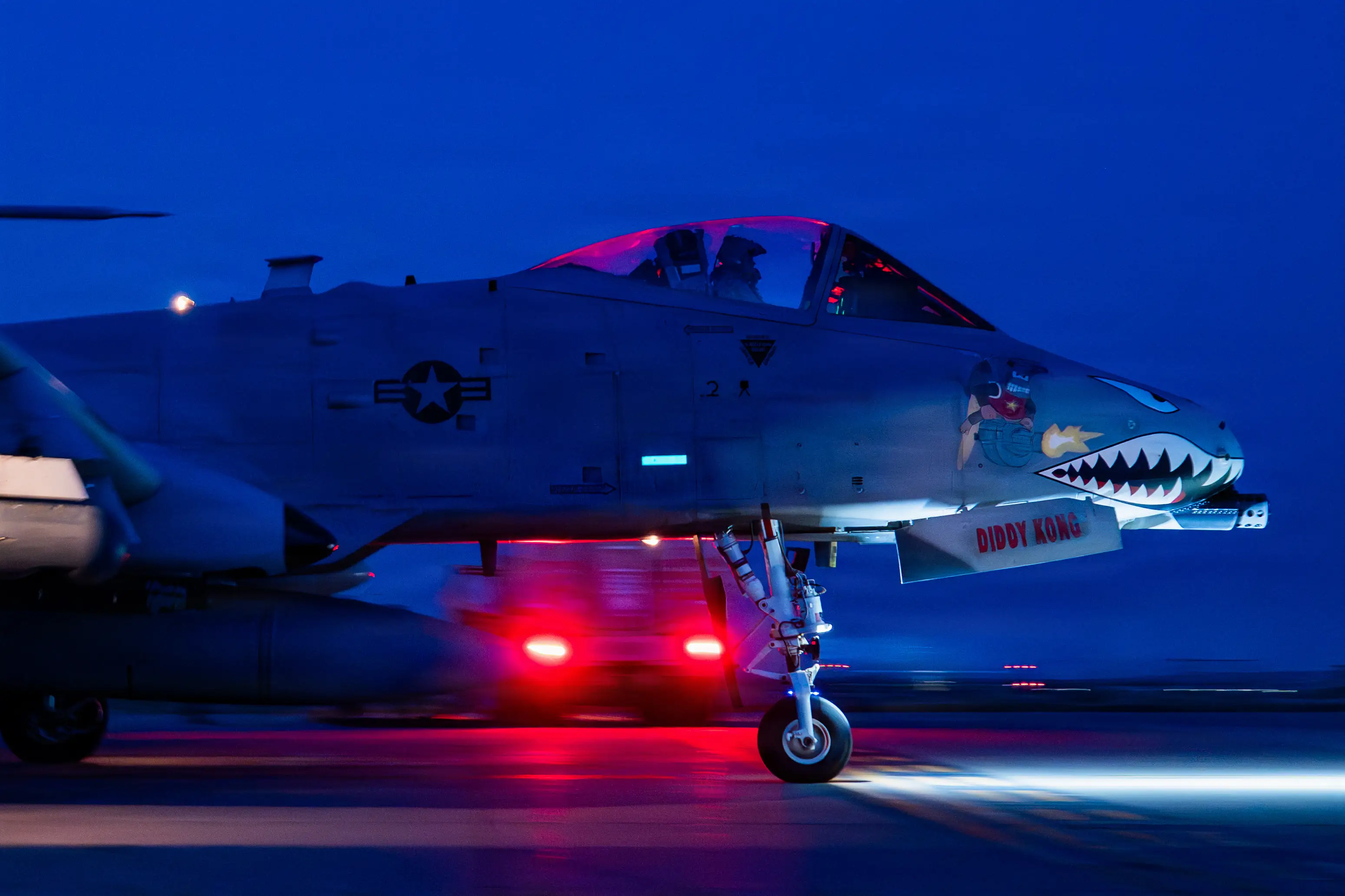 An A-10 Thunderbolt II sits on a tarmac at night.