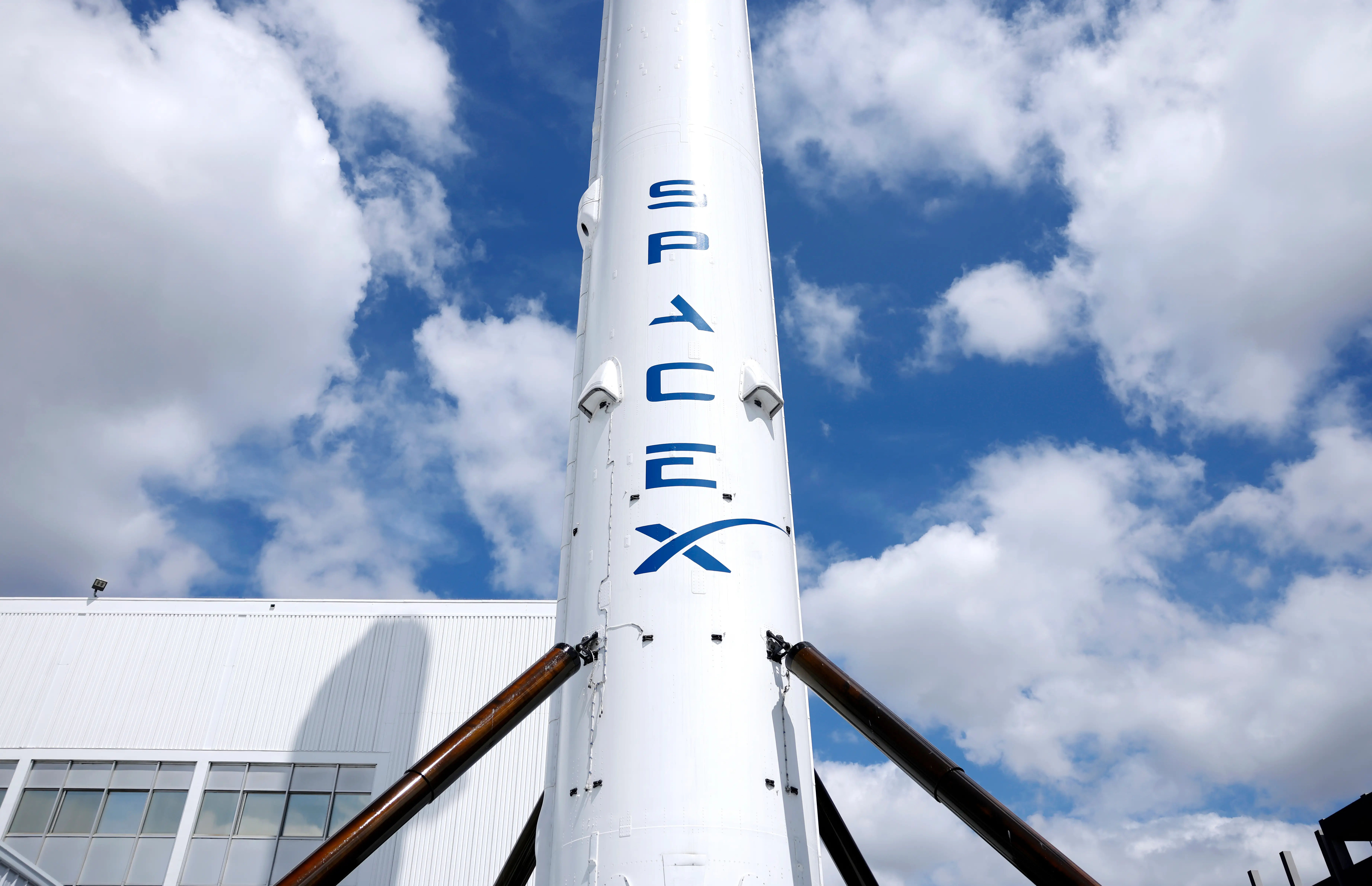A tube with SpaceX's blue logo is held up by four metal joists.