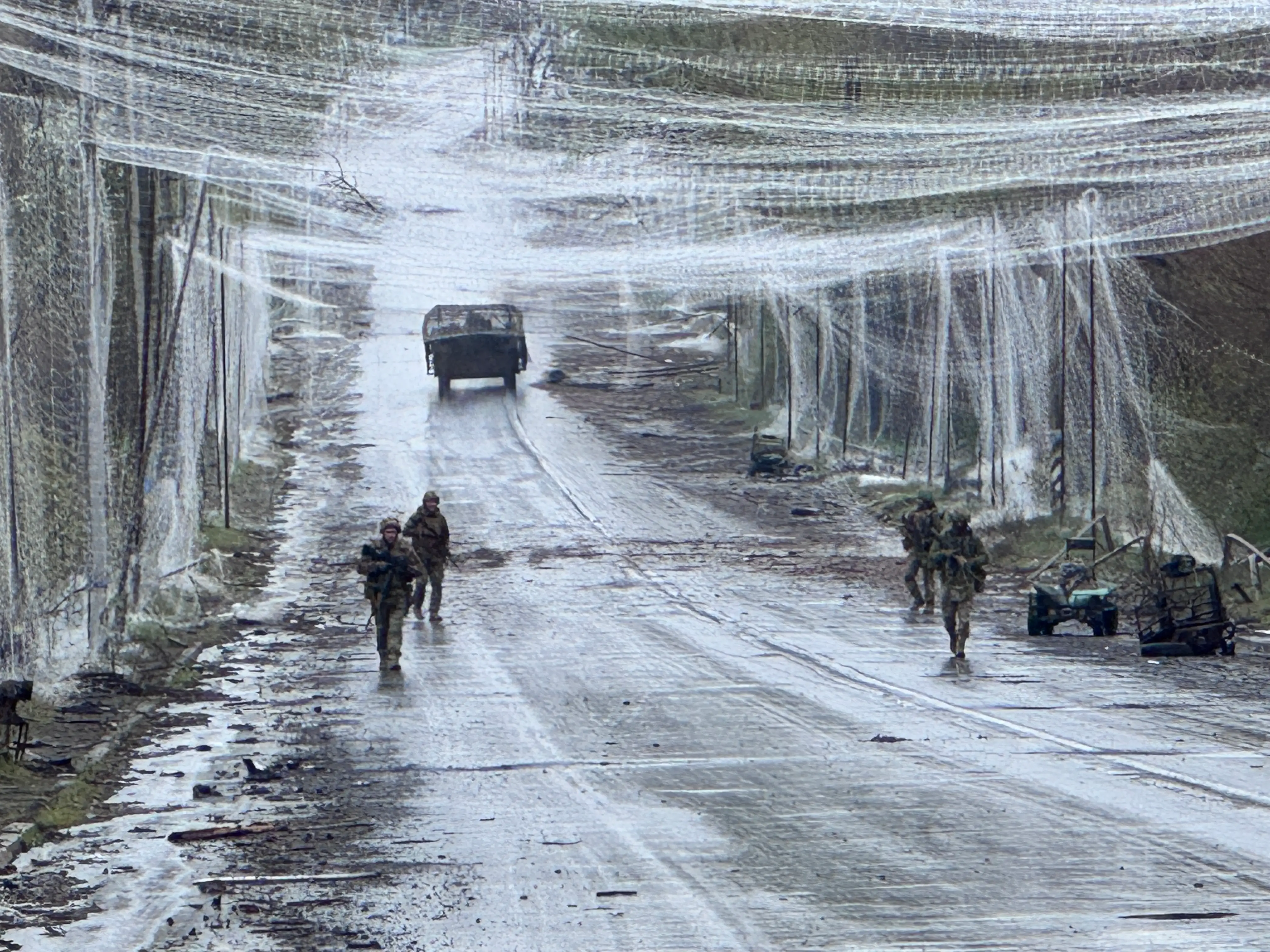 Ukrainian infantry walk along a road covered in anti-drone netting.