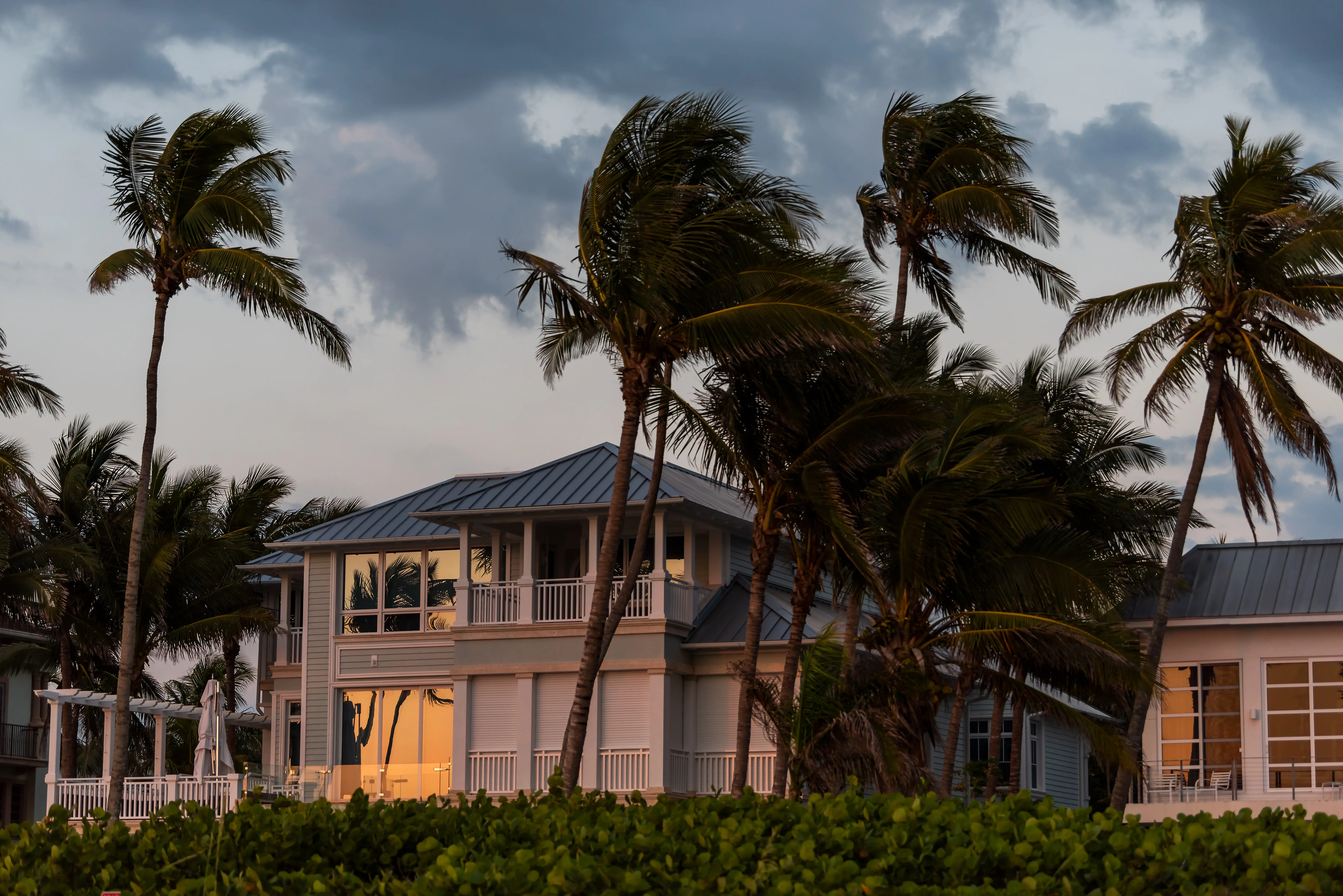 A waterfront home during evening sunset with storm weather, wind, and palm trees.