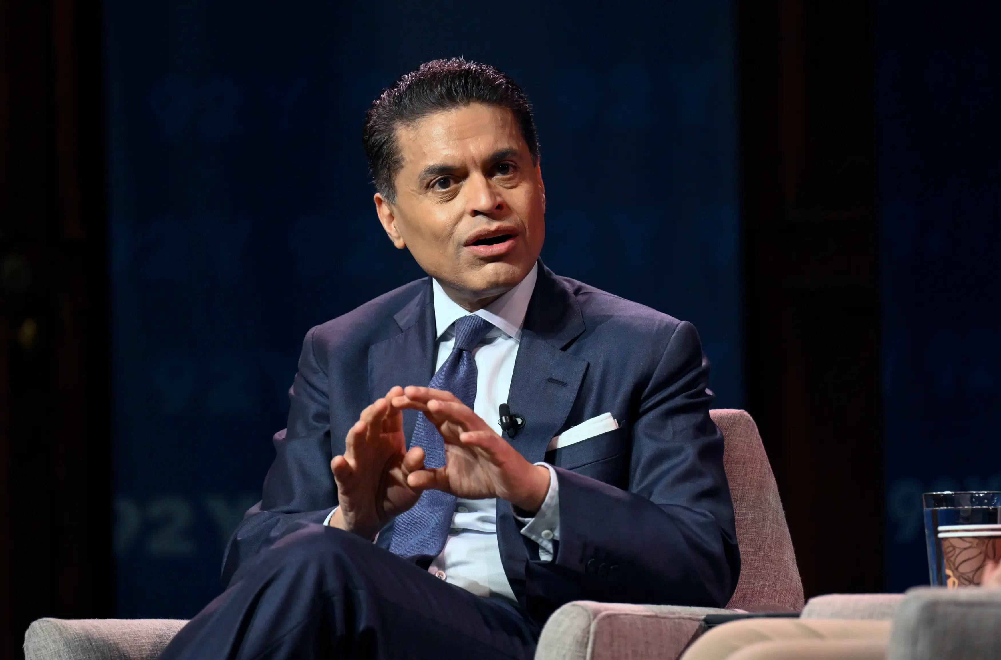 Fareed Zakaria, dressed in a navy suit with a blue tie, talks onstage.