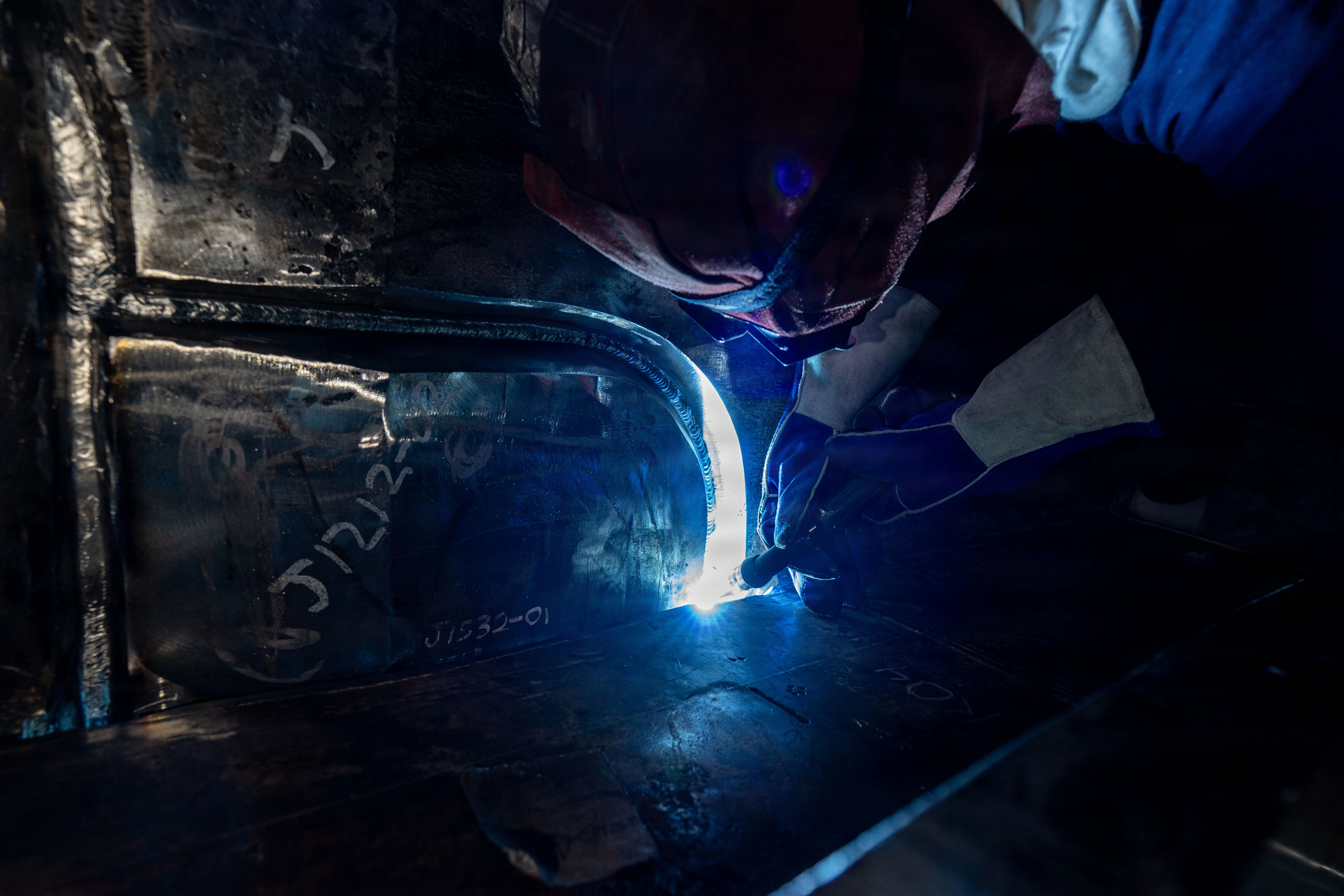 A shipbuilder grinds a piece of metal in a submarine.