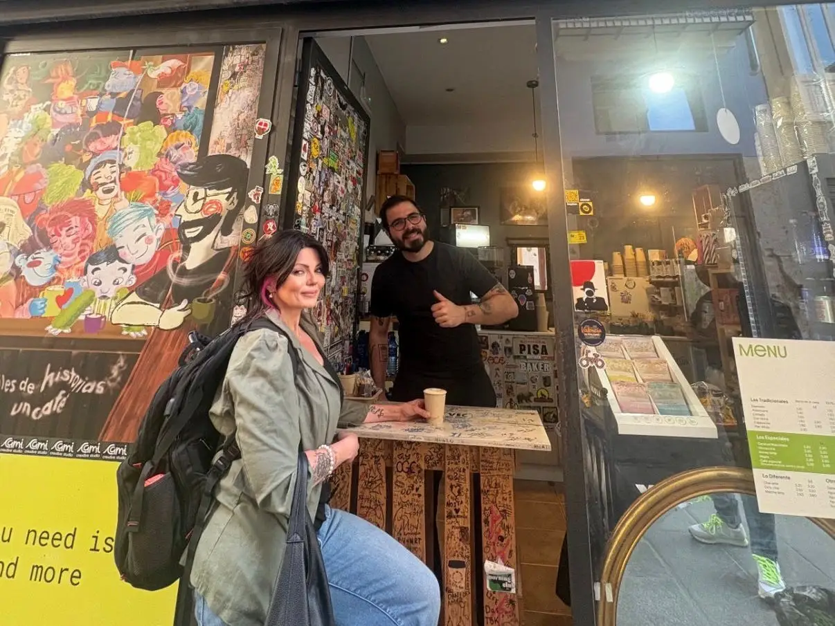 A woman standing outside a coffee bar with a barista inside