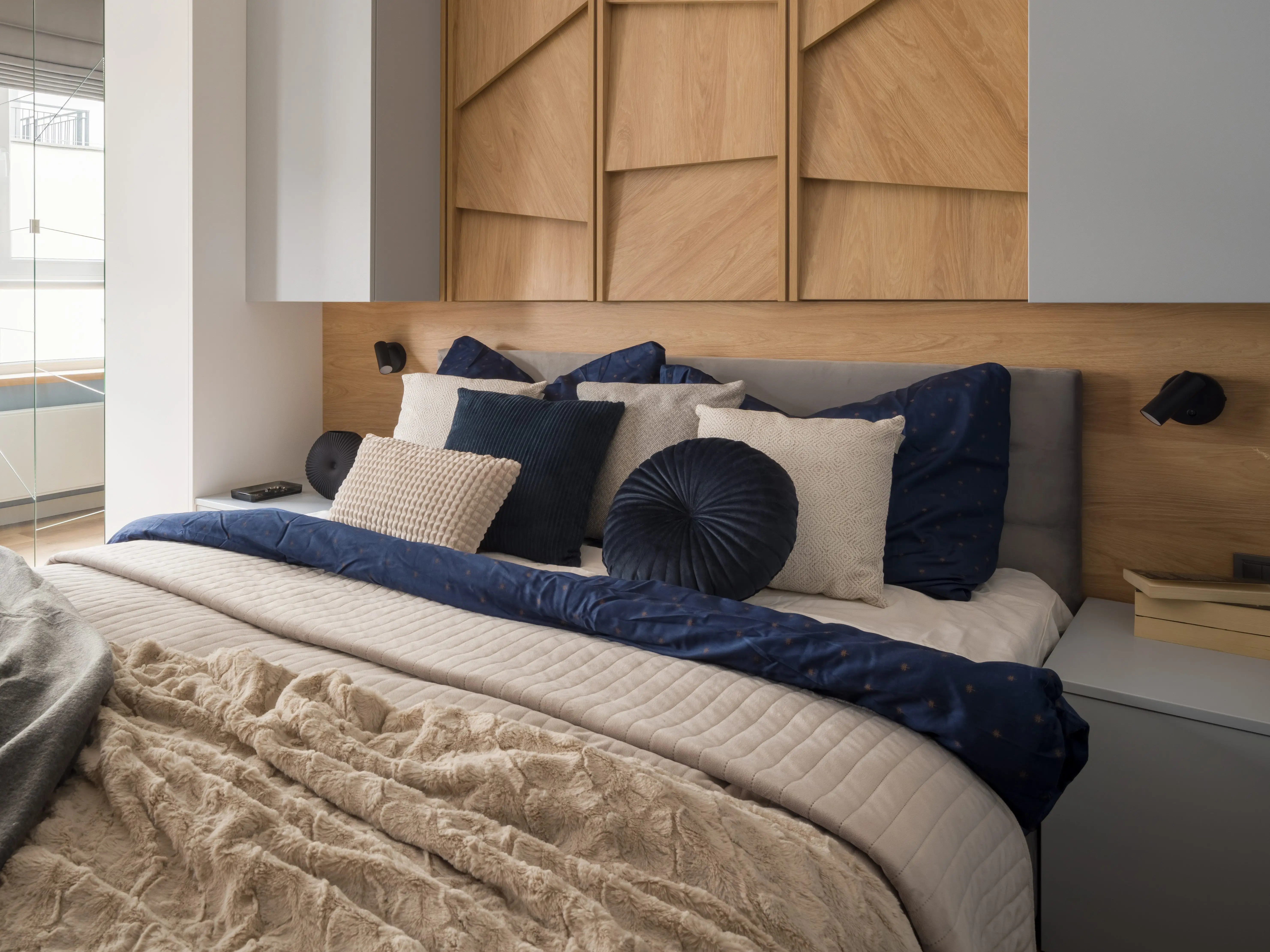 Large built-in headboard with wood behind bed topped with navy, white, and gray throw pillows of various sizes