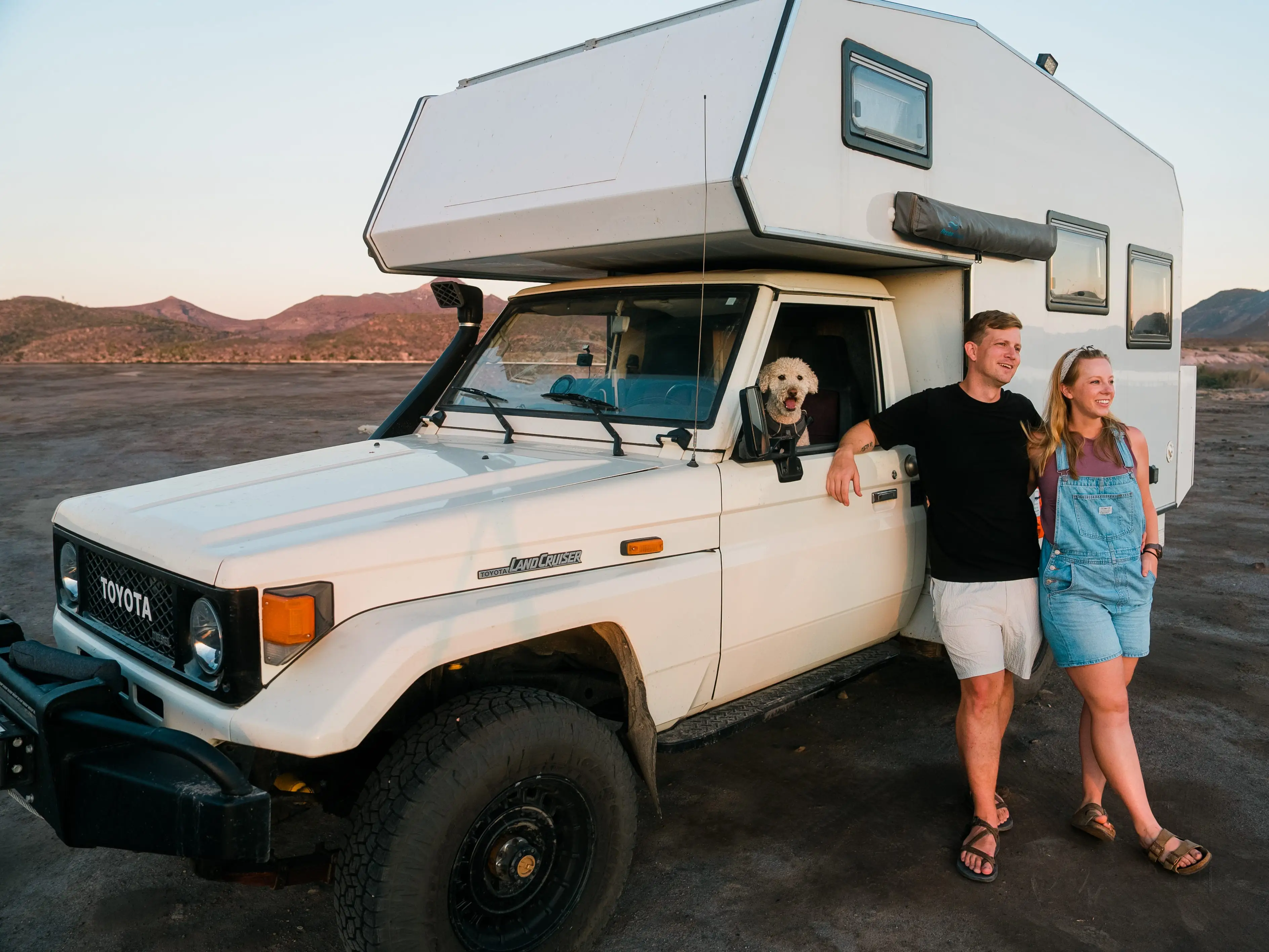 Chris and sara standing outside their camper van with their dog in the front seat