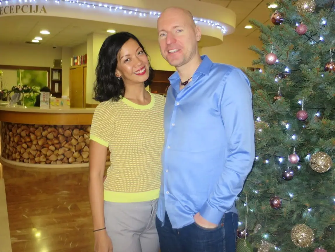 Lily Fen and her husband standing next to a Christmas tree in a building lobby.