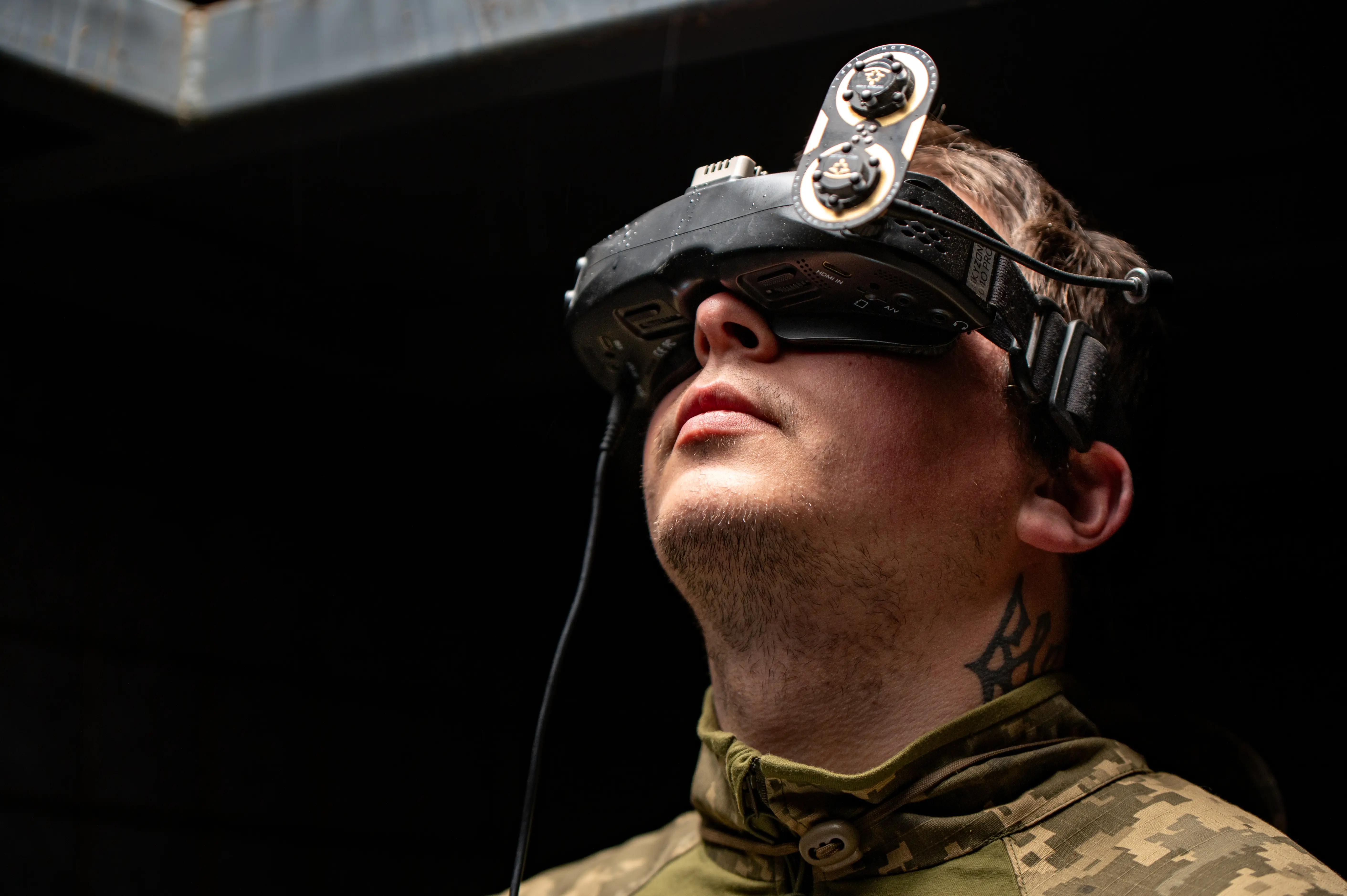 A man in khaki top looks up in a dark room with a headset over his eyes