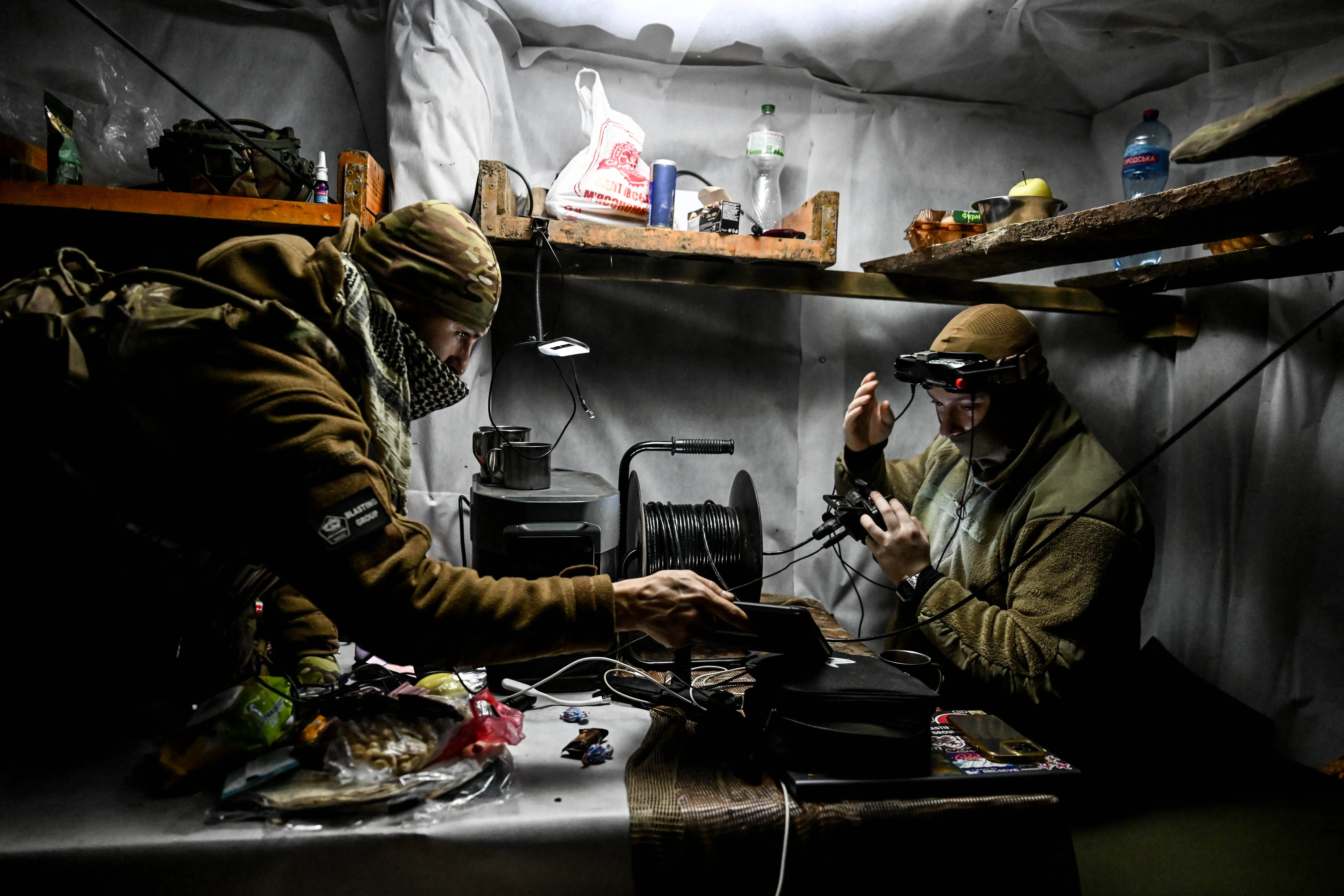 Two men in khaki in an indoor location with controllers and fiber optic spools
