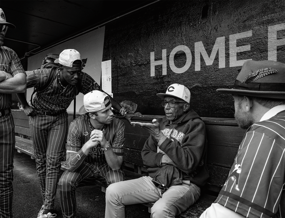 black-and-white photo of older man sitting in dugout surrounded by other players listening to him speak