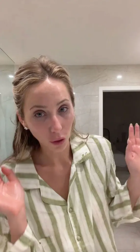 Alix Earle in a green and white striped shirt, applying skincare products to her face, with hands raised, speaking to the camera.