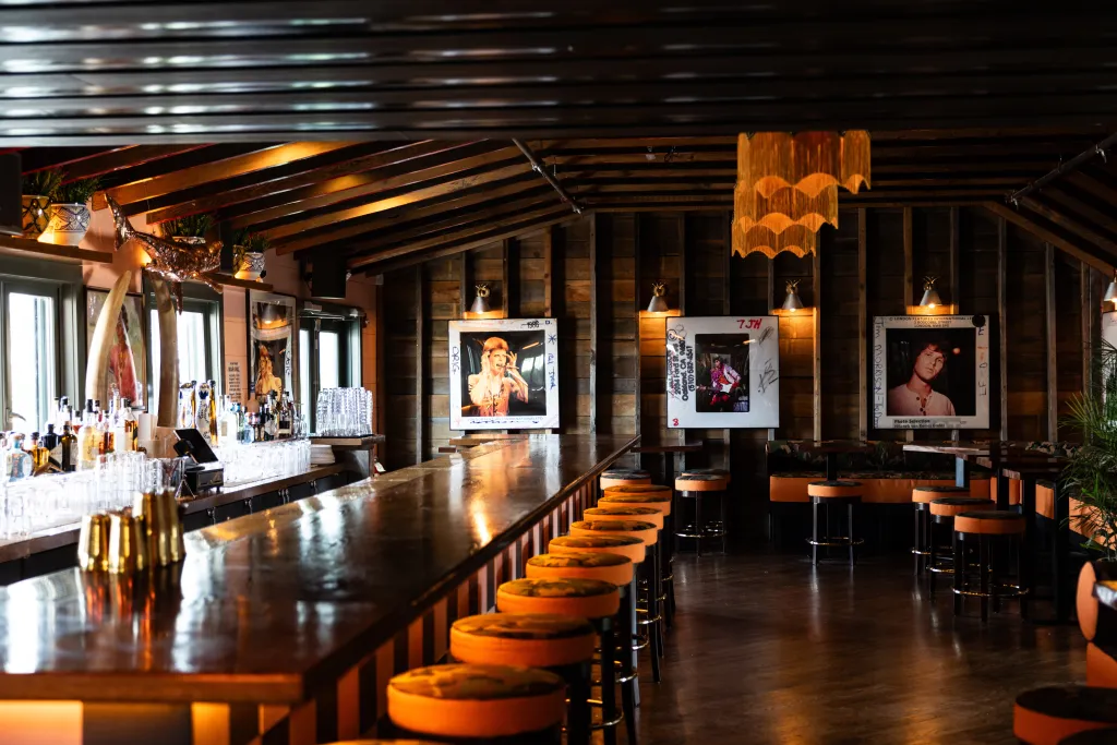 The interior of Mary Lou's, featuring a long wooden bar with orange-seated stools, and three framed black and white portraits of musicians on the back wall.