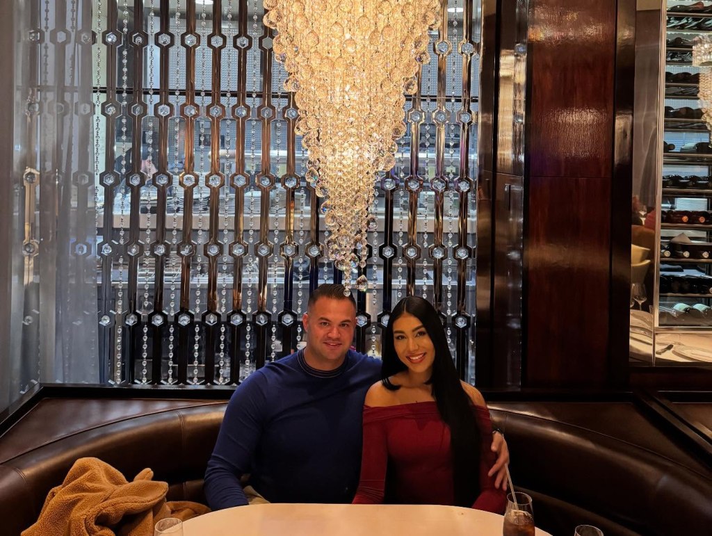 Patrick Mendes and Thais Ramone sitting in a restaurant booth under a chandelier.