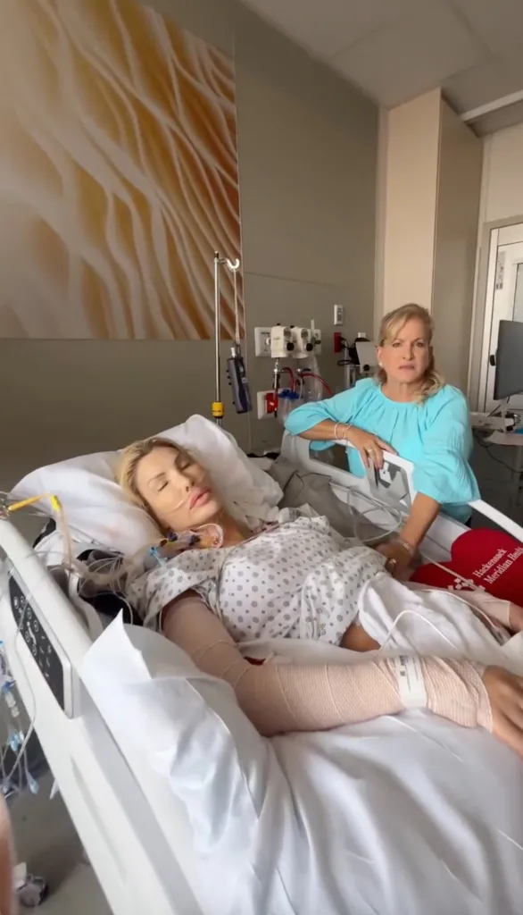 Nikki Exotica in a hospital bed with medical tubes and wraps, and her mother standing beside her.