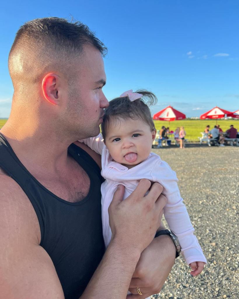 Patrick Mendes holding his daughter, who sticks her tongue out.