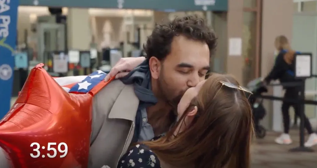 A man and woman kiss, with a red star balloon and US flag visible.