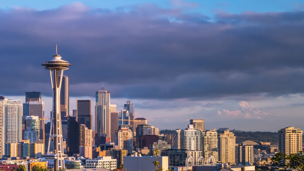 The Seattle skyline featuring the Space Needle and buildings, with Mount Rainier visible in the distance under a dramatic sky.