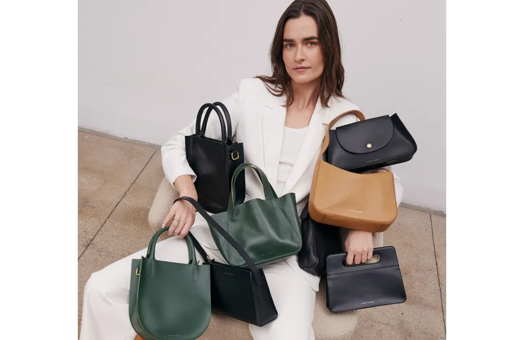 A person in a white suit holding multiple handbags in black, green, and tan colors.