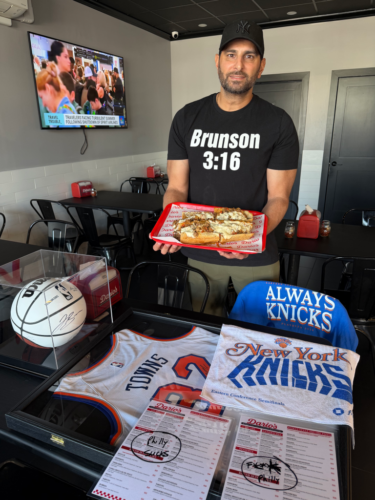 A man holding a tray of sandwiches in a restaurant displaying Knicks basketball memorabilia.
