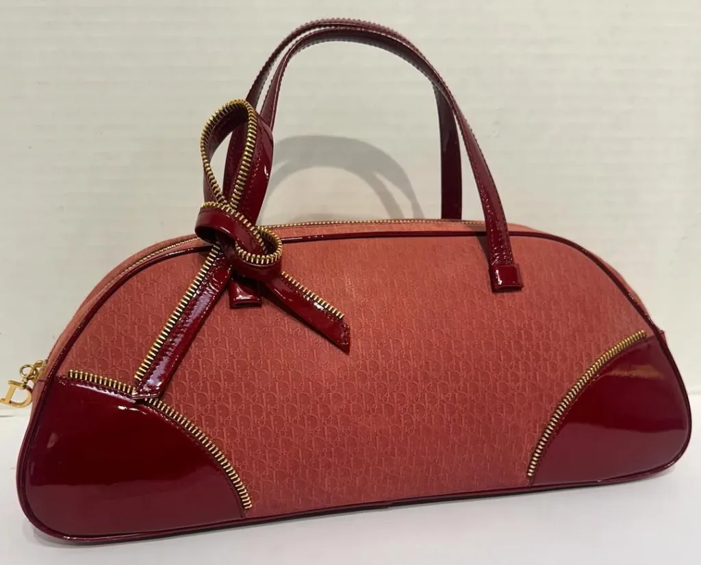 A coral and burgundy patterned handbag with patent leather trim and a bow made of zipper.