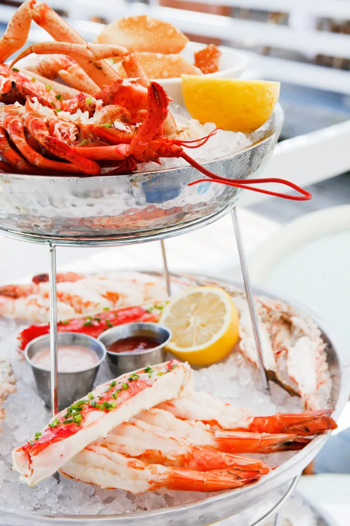Seafood tower with lobster, crab legs, shrimp, lemon wedges, and sauces on ice.