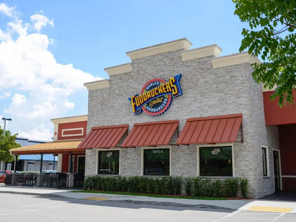 The exterior of a Fuddruckers restaurant with a stone facade, red awnings, and a sign advertising 