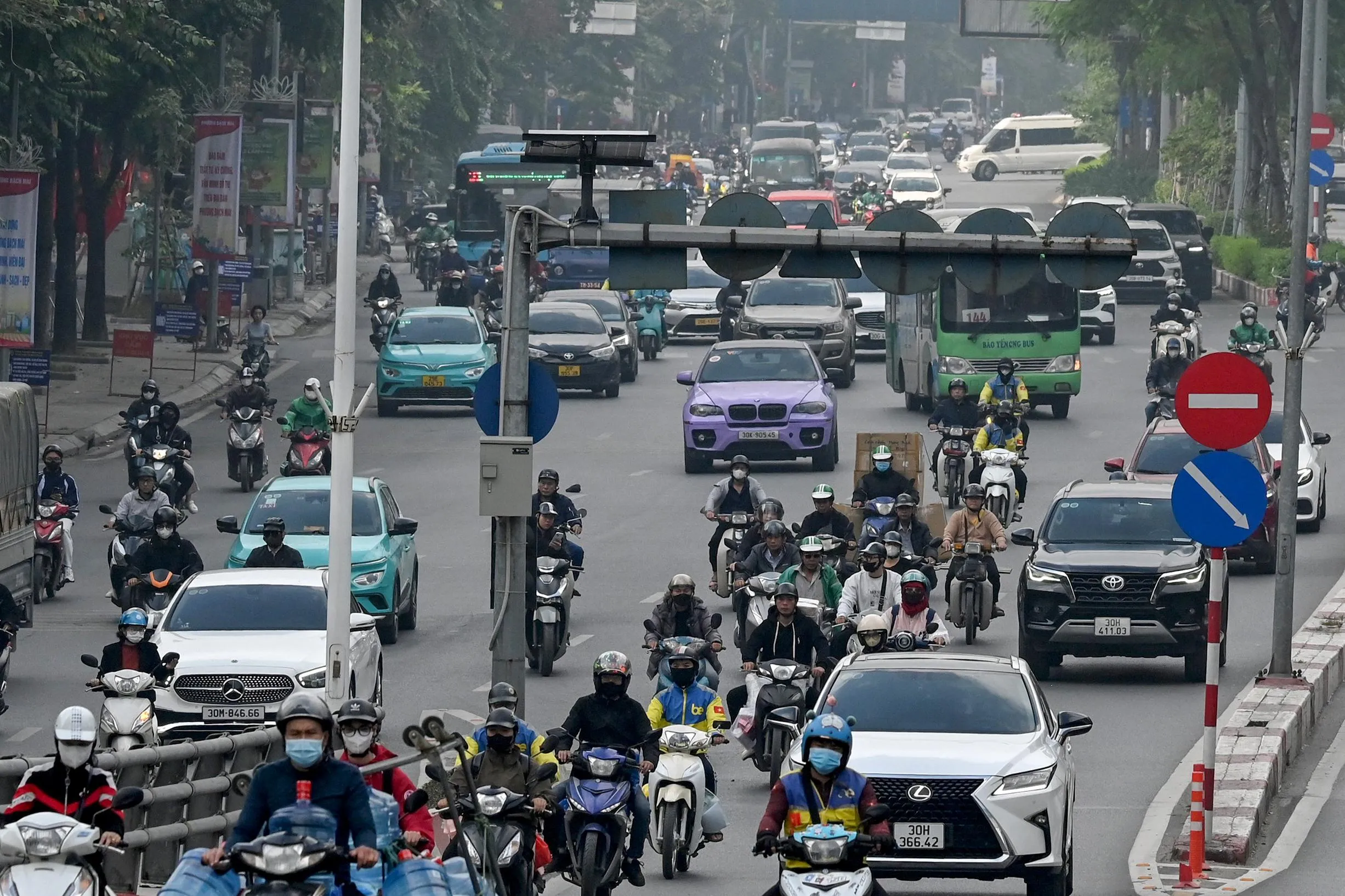Dense urban traffic of motorbikes, cars, taxis, and buses fills a hazy multilane street, with riders packed closely together in mixed traffic. Dense urban traffic of motorbikes, cars, taxis, and buses fills a hazy multilane street, with riders packed closely together in mixed traffic.