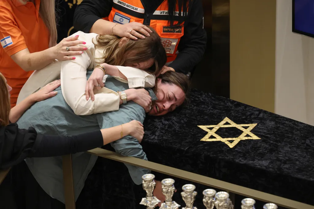 Family crying over they casket of Eli Schlanger, which is draped with a Star of David