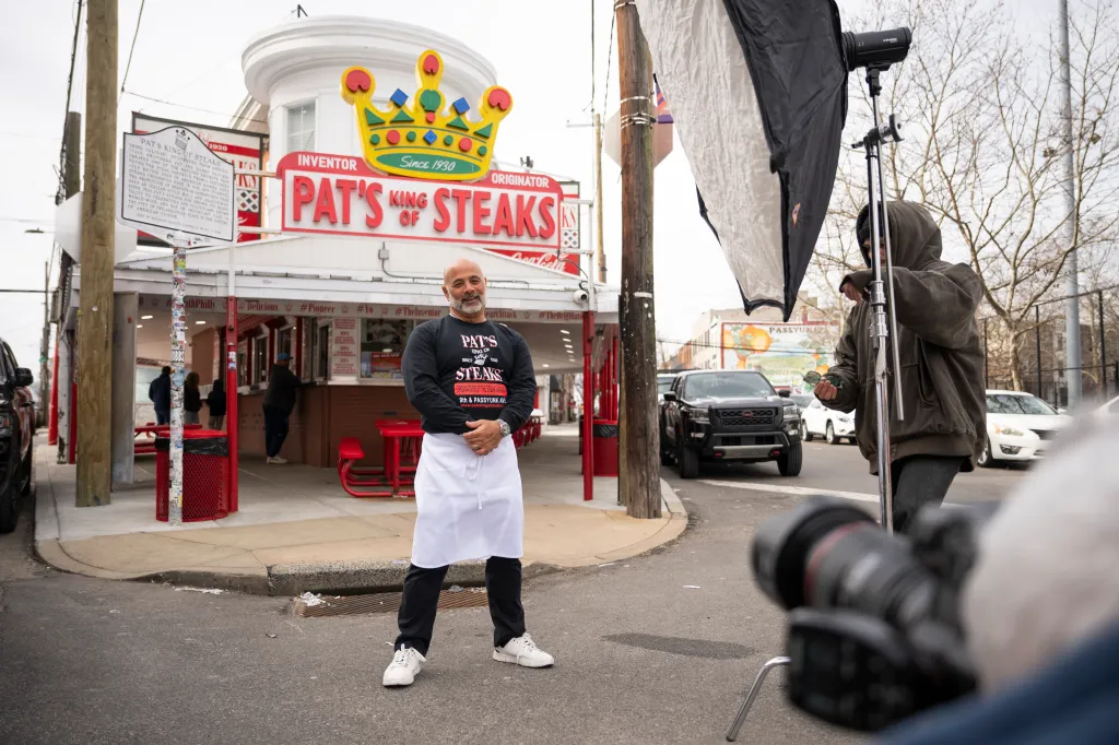 The owner of Pat's King of Steaks poses outside his cheesesteak shop while being photographed.