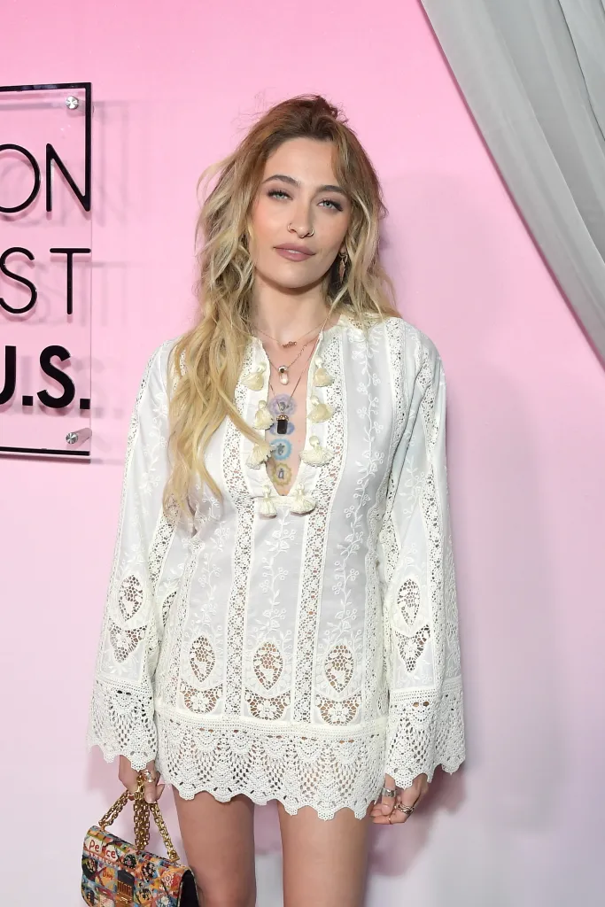 Paris Jackson wearing a white embroidered dress with fringe and holding a colorful patterned purse.