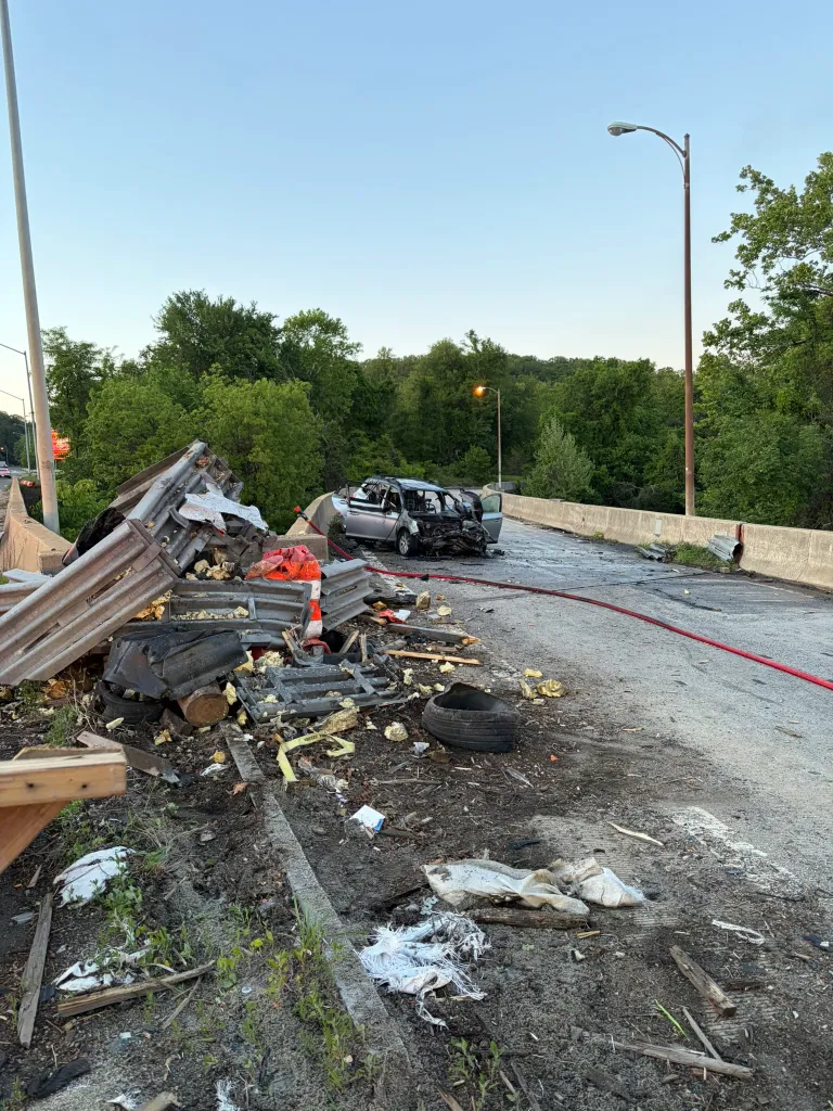 The scene of a severe car accident on a road next to a guardrail and trees.